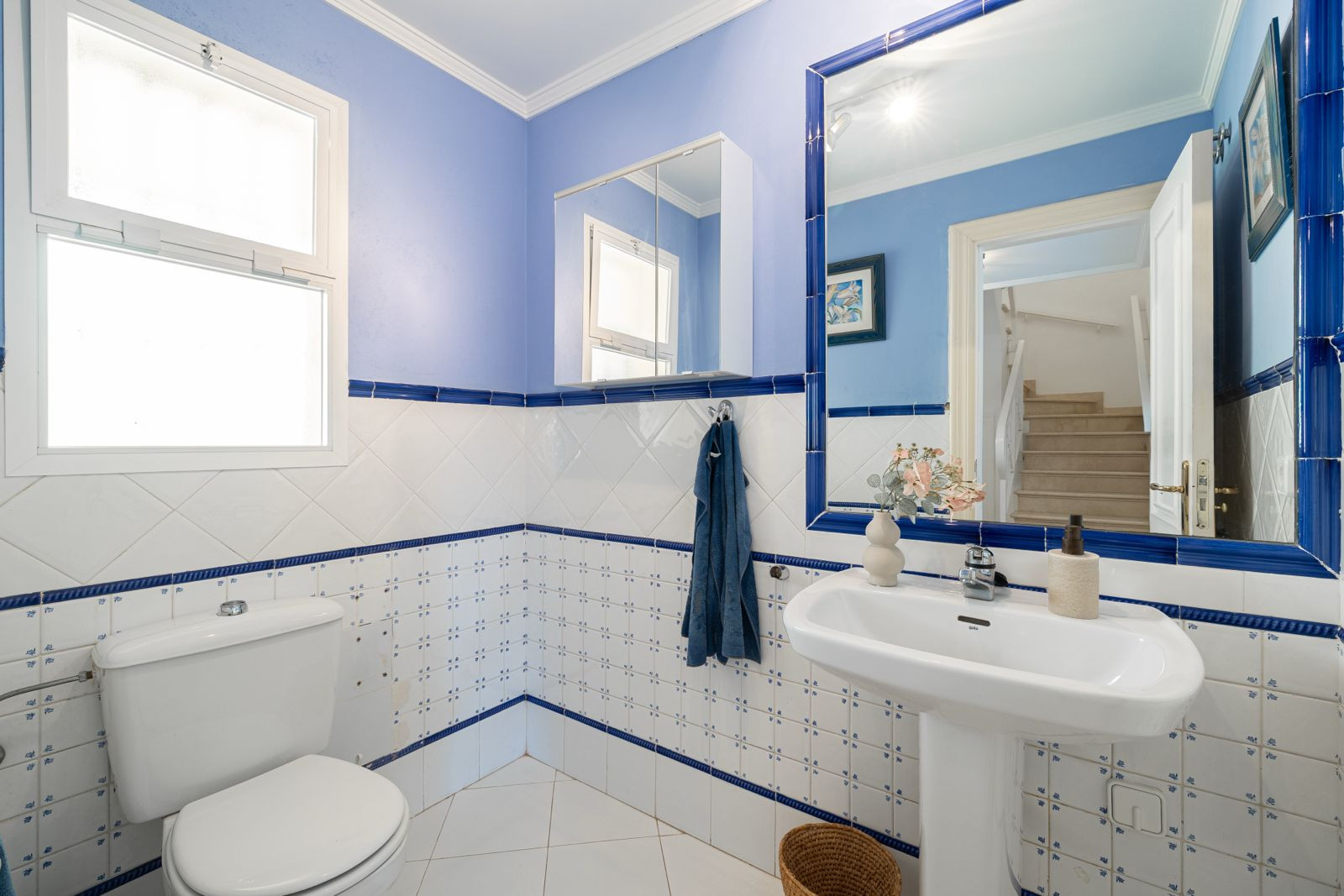 Blue bathroom with sink, mirror, and towel hanging on the wall.