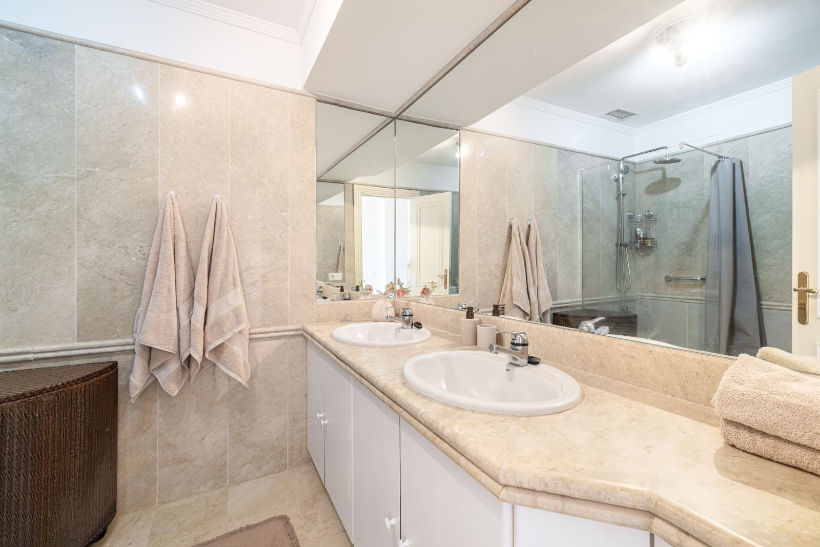 Master bathroom with dual sinks, marble walls, mirrors and a glass shower.