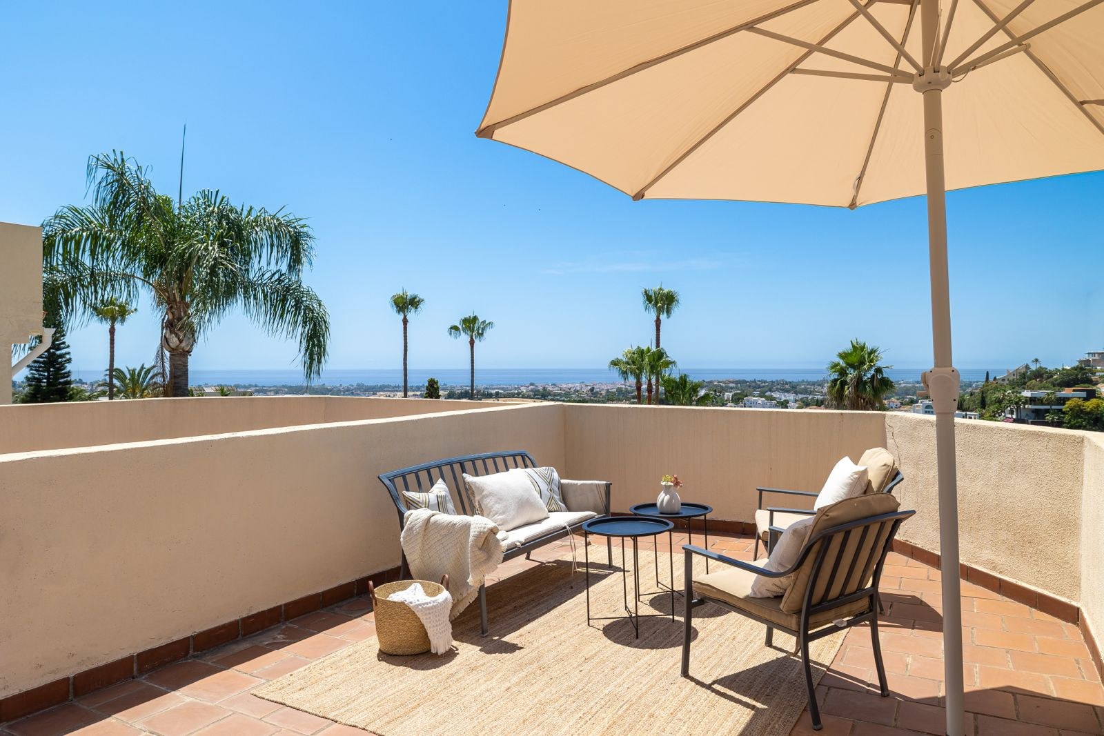 Outdoor terrace with seating, palm trees, and a view of the coastline.