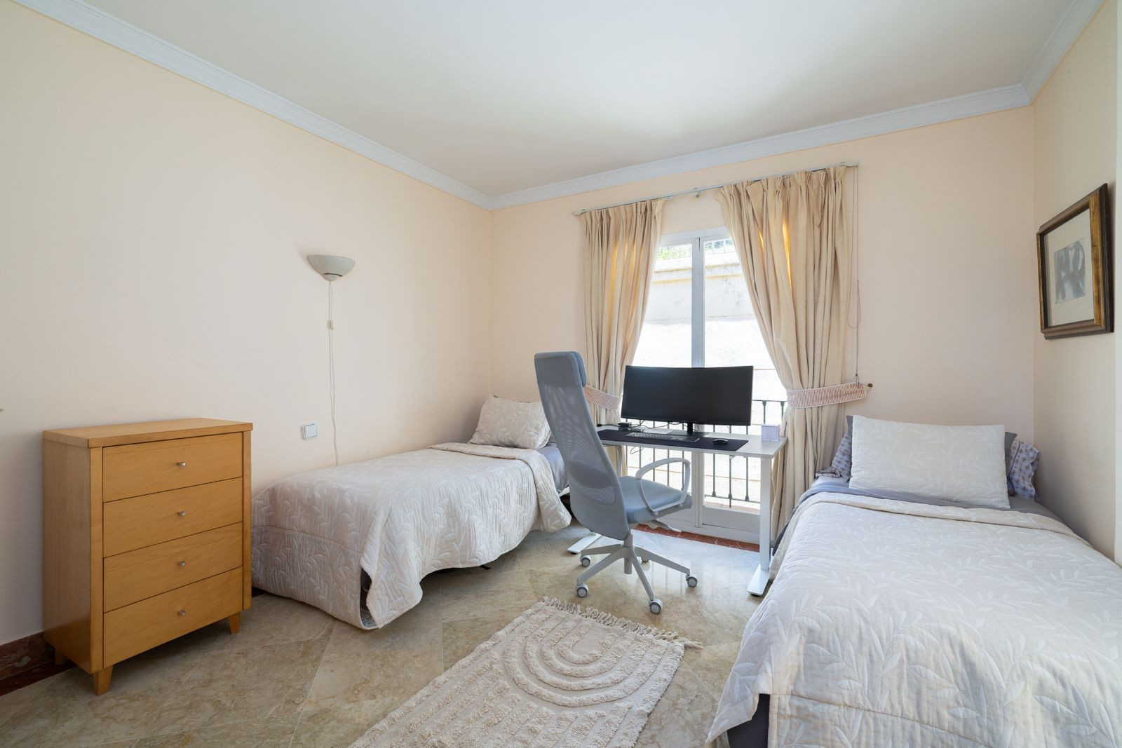 Bedroom with two single beds and a desk facing a window.