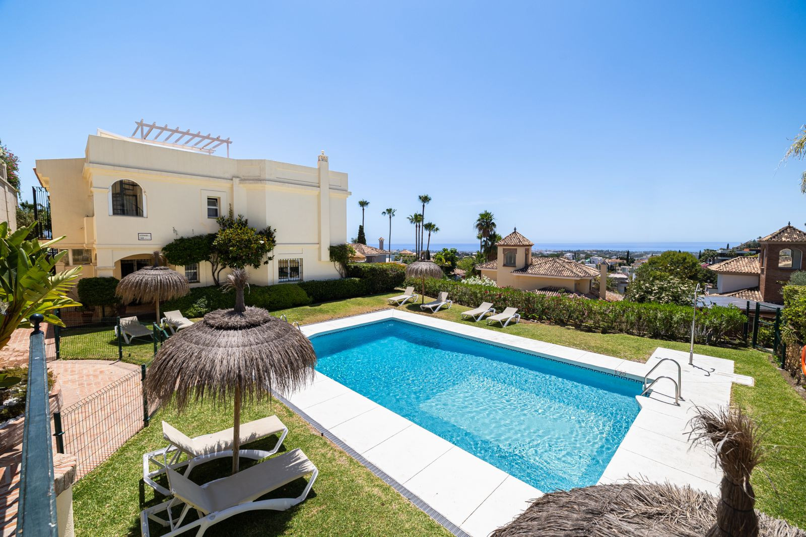 Outdoor pool area with sun loungers, umbrellas, and garden view.