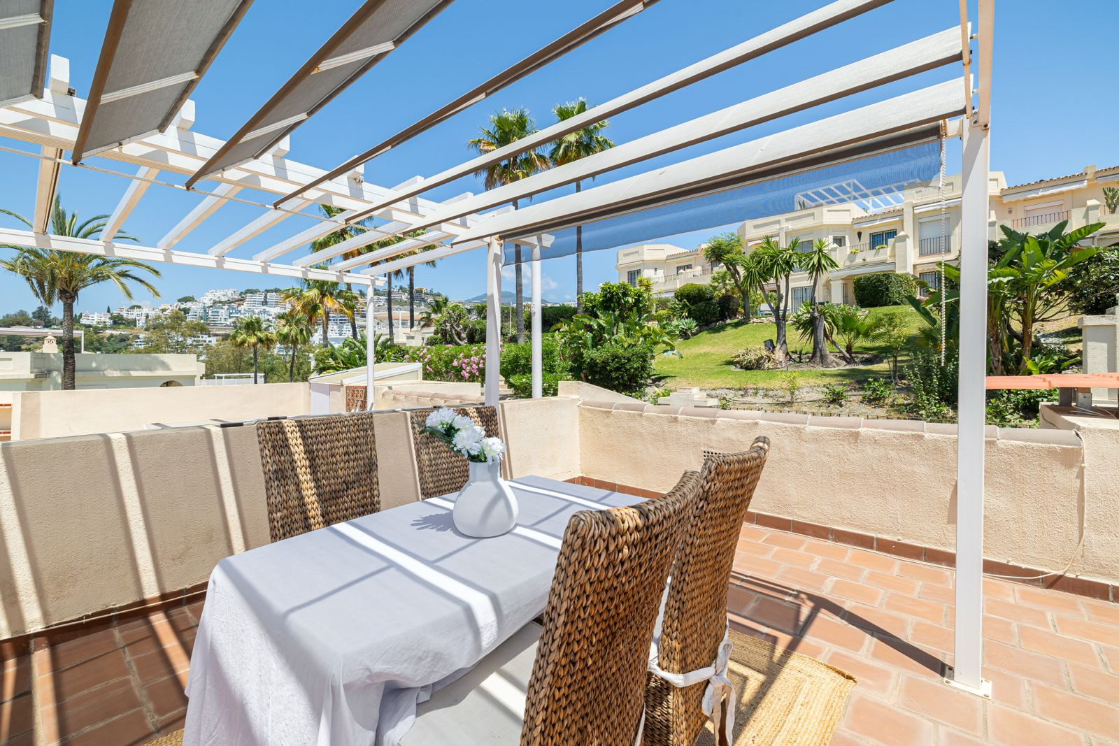 Dining area on terrace showing a white table, chairs, and nearby greenery.