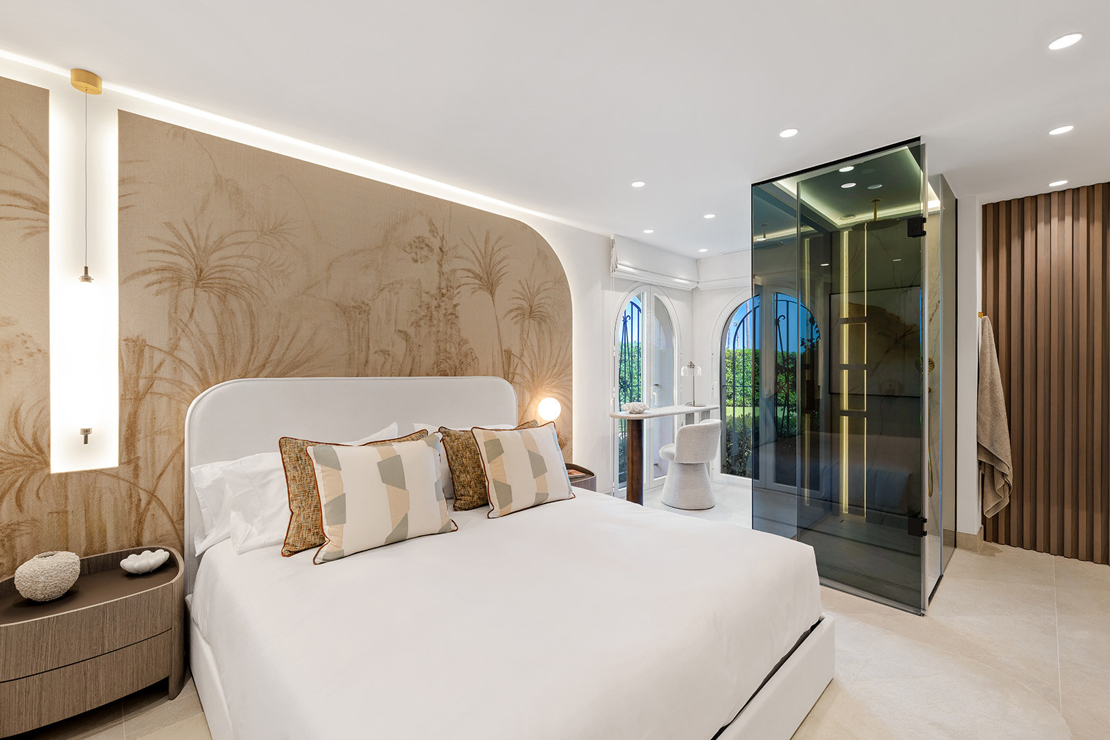 Bedroom with a large bed, decorative wall art, glass shower enclosure, and arched window views.