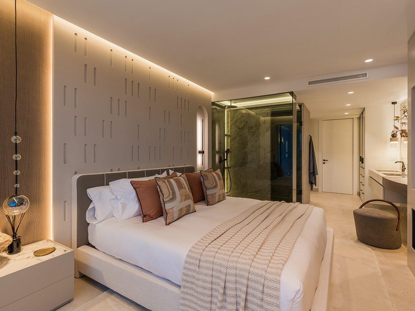 Bedroom with a large bed, textured wall, and a glass-enclosed shower area in the background.