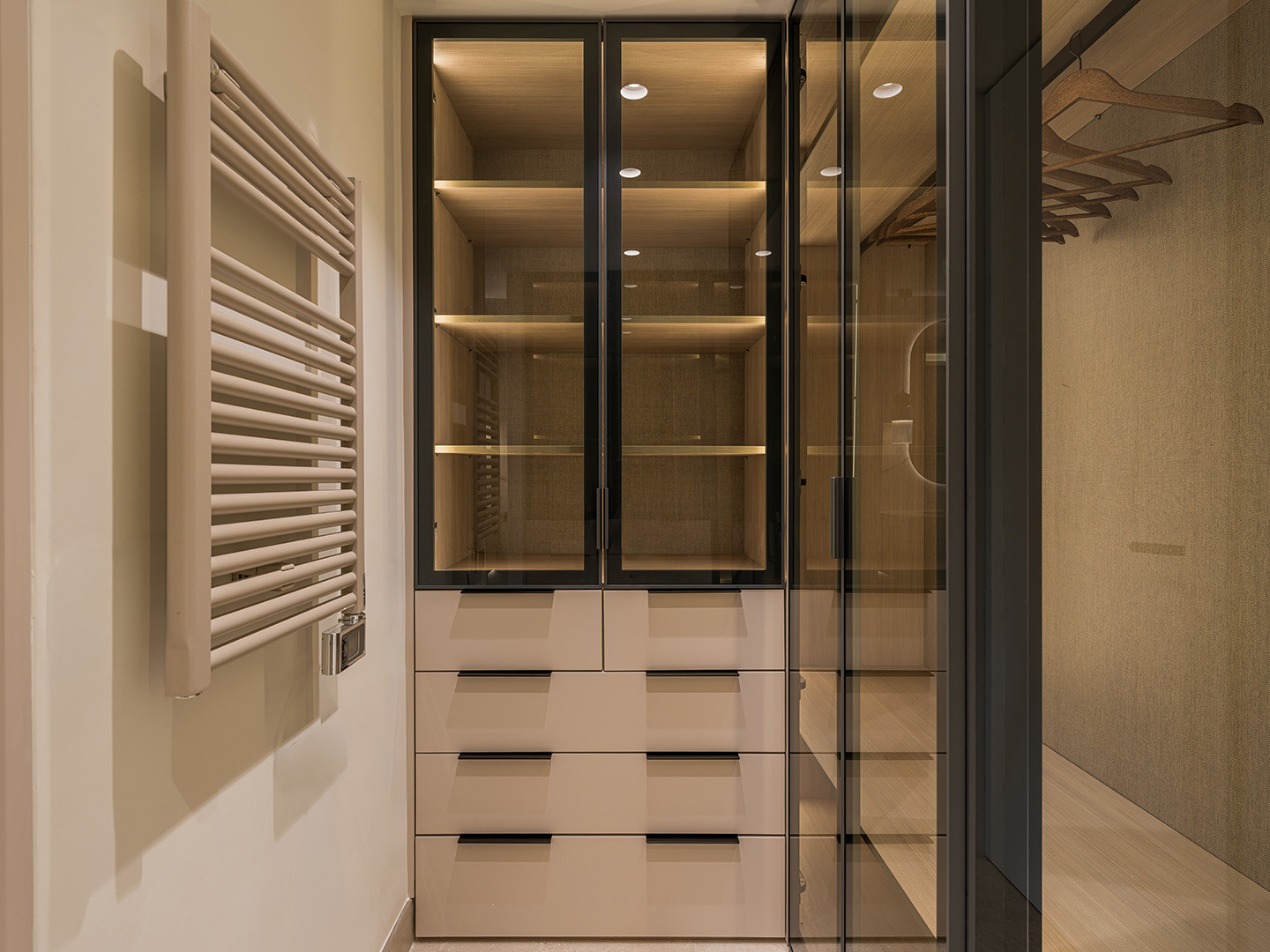 Walk-in closet with glass-front cabinets, drawers, clothes hangers, and a heated towel rail.