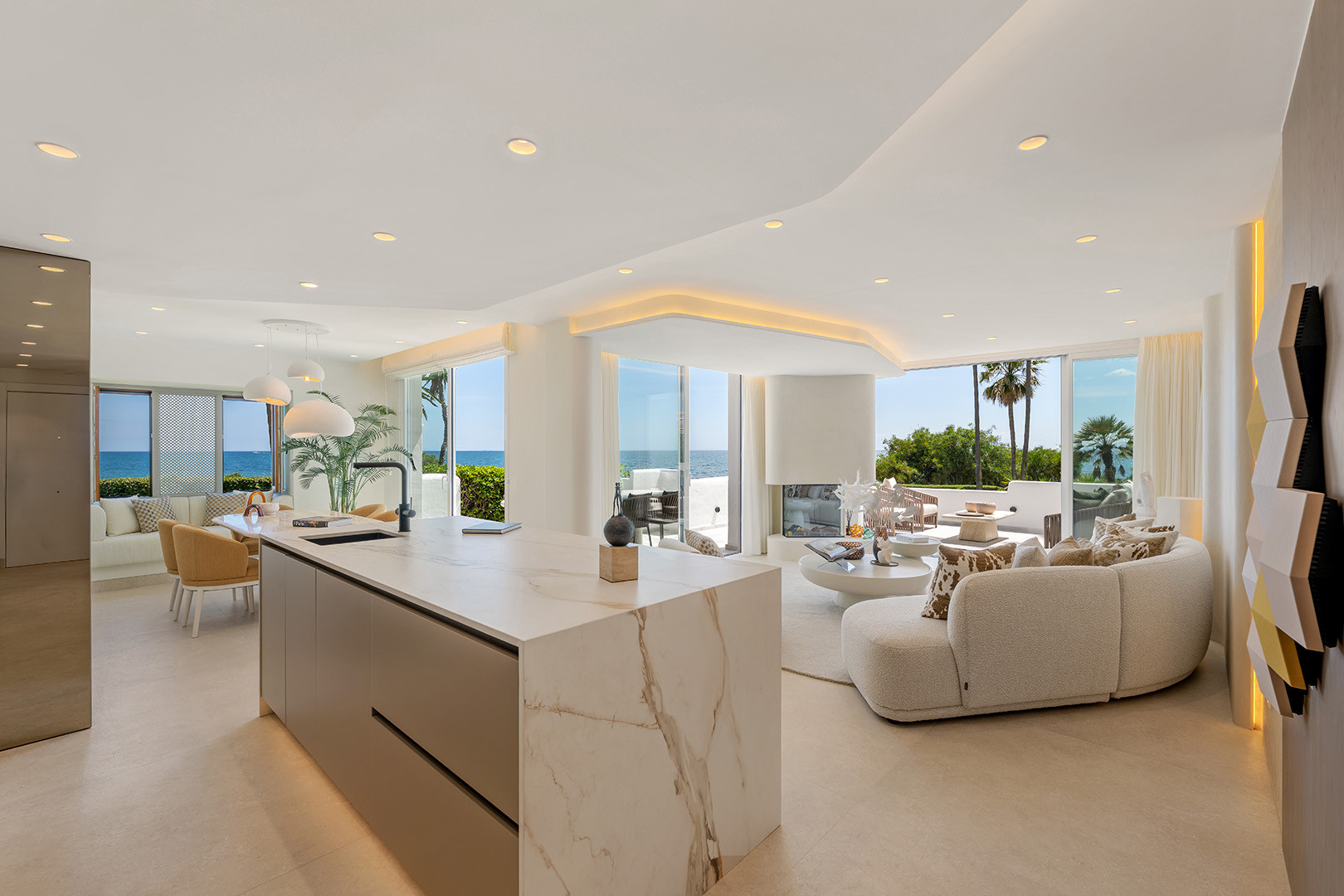 Open concept living area with kitchen island, seating, fireplace, and ocean views through panoramic windows.
