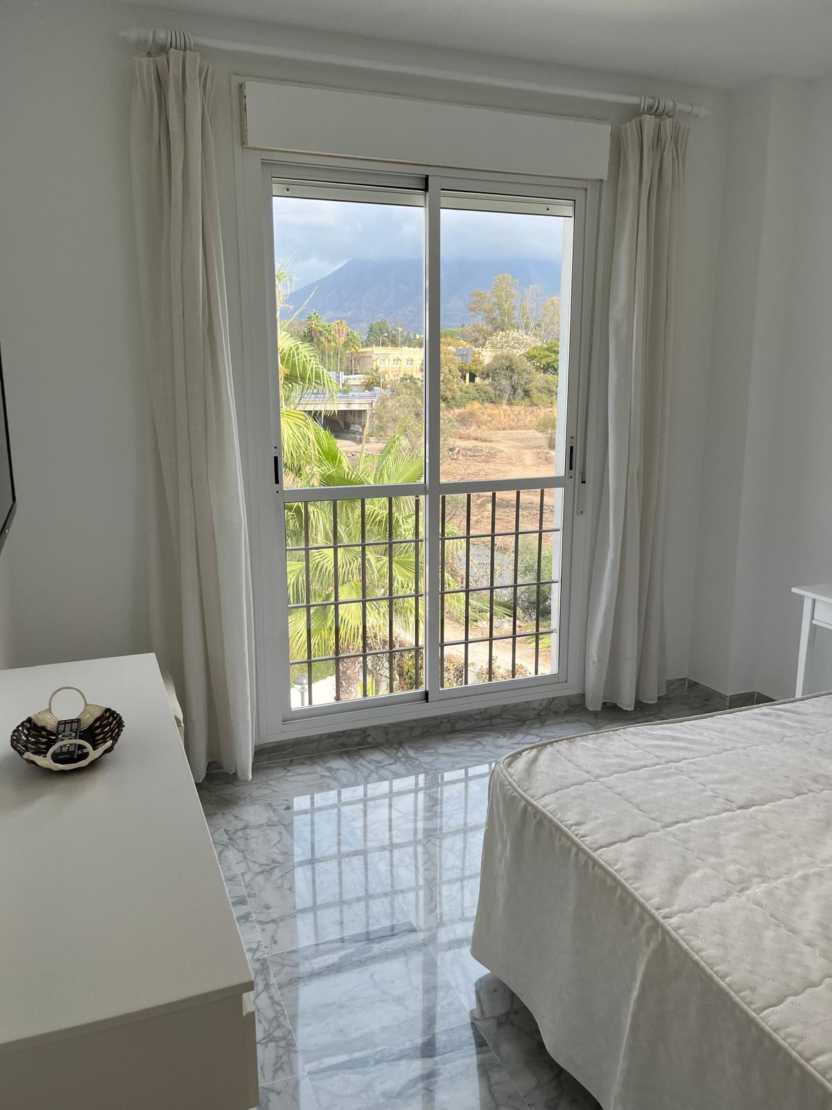 Bright bedroom with marble floors and mountain view through large window.