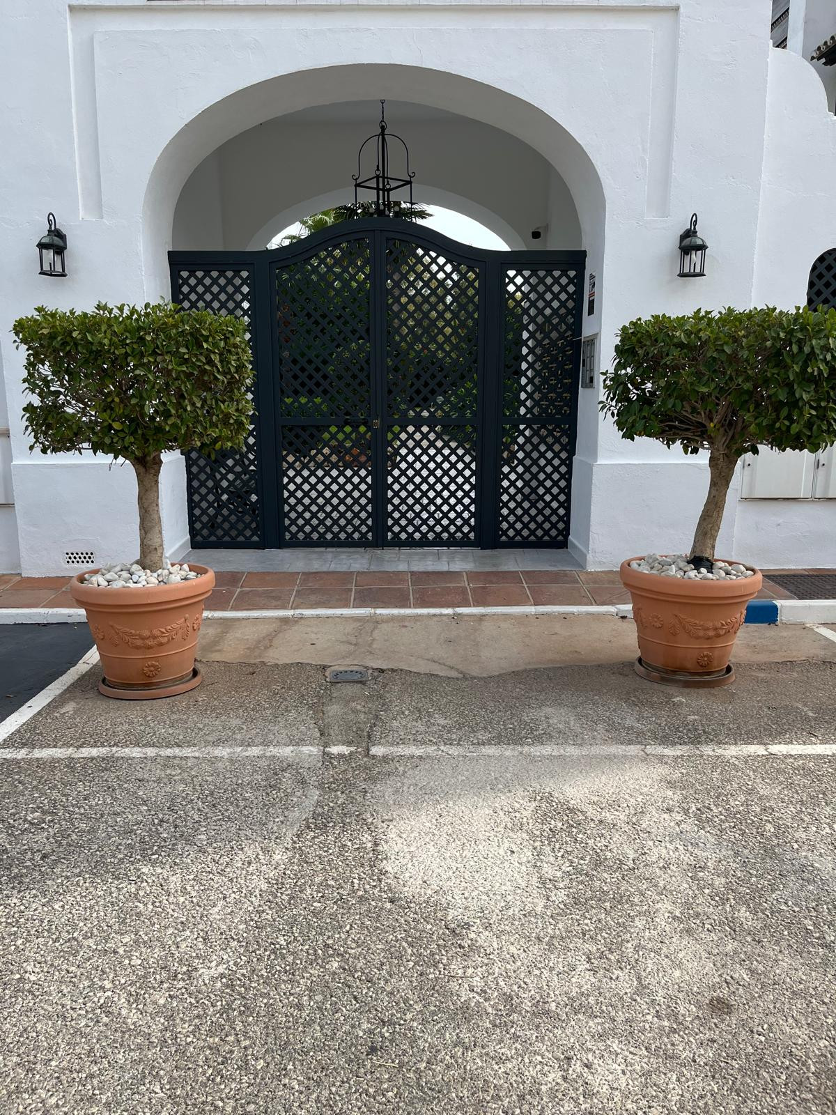 Exterior view of a gated entrance with potted trees on both sides.