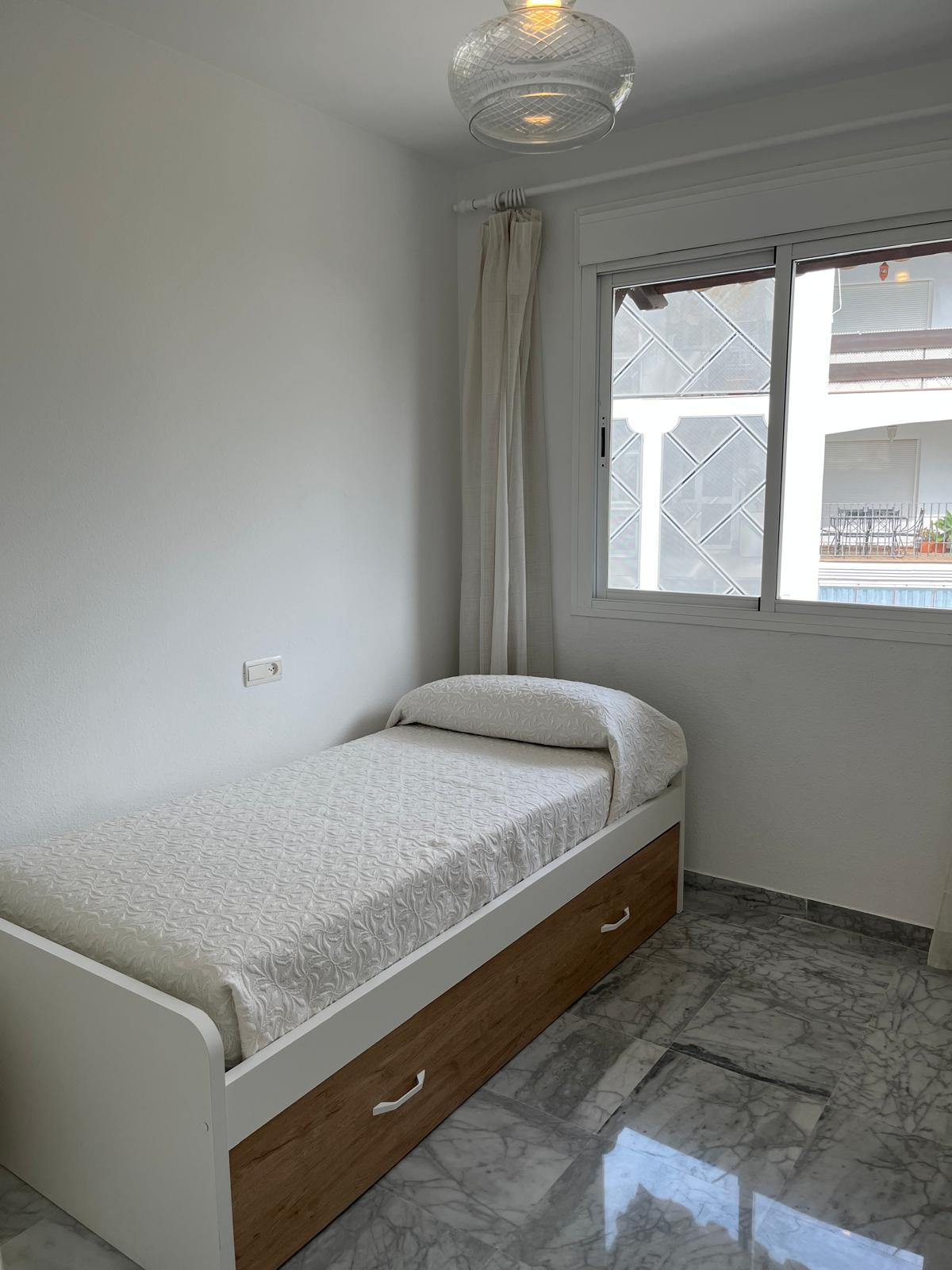 View of single bed in second bedroom, decorated with light-colored linens.