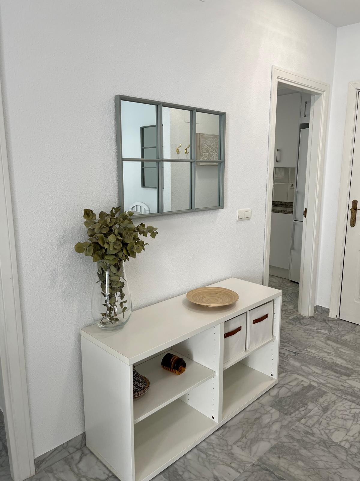 Hallway with console table, mirror, and decorative vase against a white wall.
