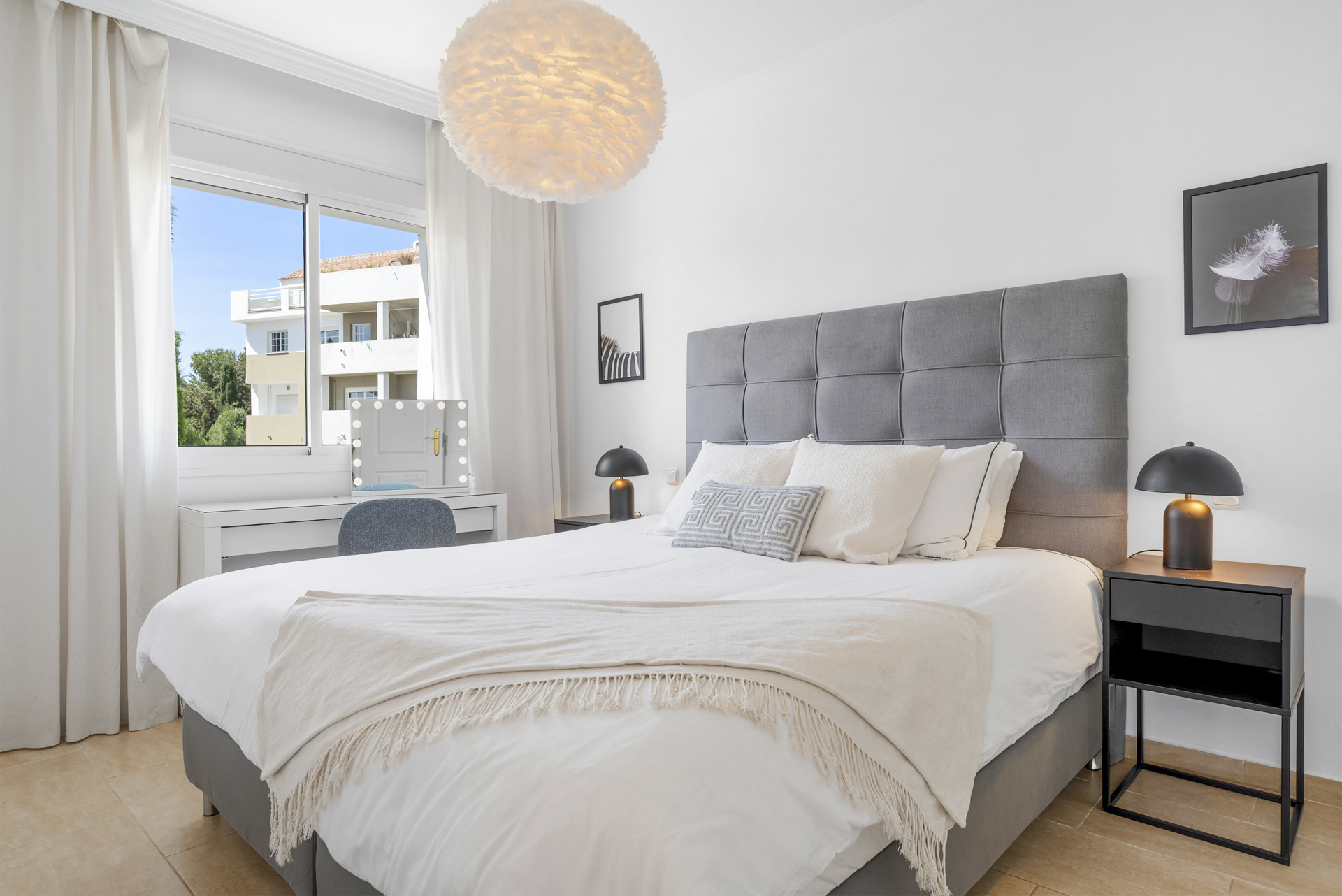 Spacious bedroom featuring a large bed, a stylish light fixture, and a vanity area with a mirror.