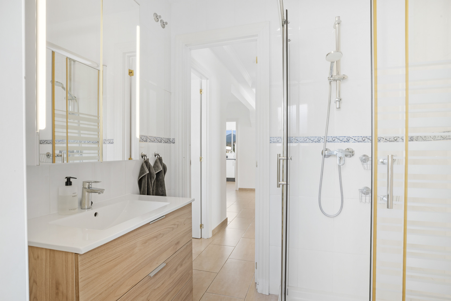 Contemporary bathroom with a glass shower, wooden vanity, and dual mirrors reflecting a bright interior.