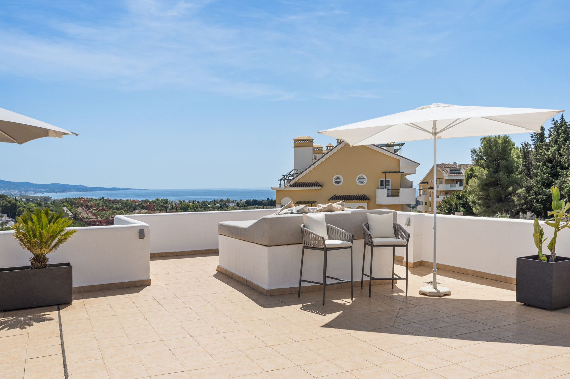 Terrace with sun umbrellas and seating area overlooking the sea and landscape.