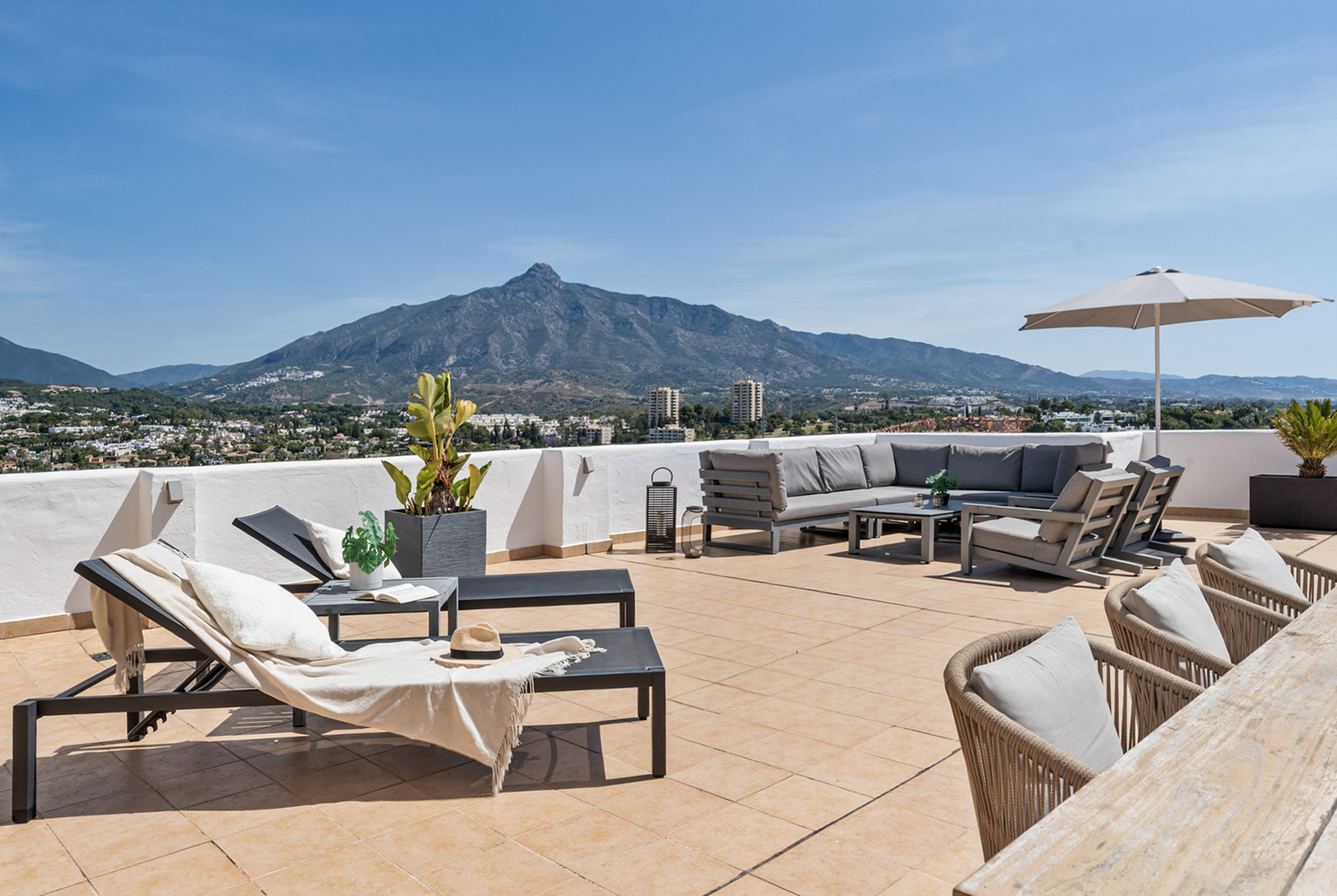 Spacious terrace with loungers, seating area, and panoramic mountain views under clear skies.
