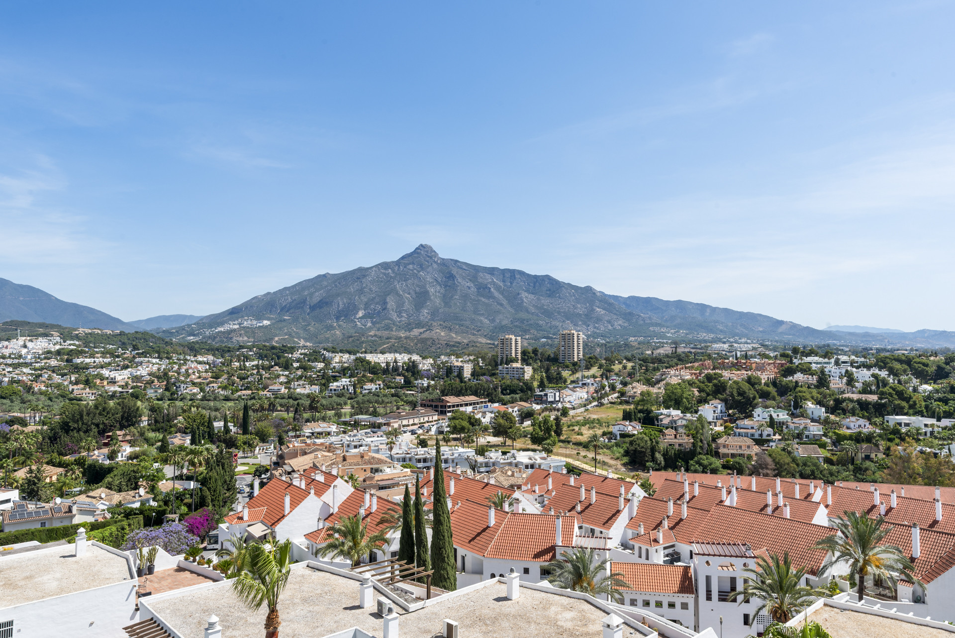 Panoramic view showing rooftops and mountains against a clear sky.