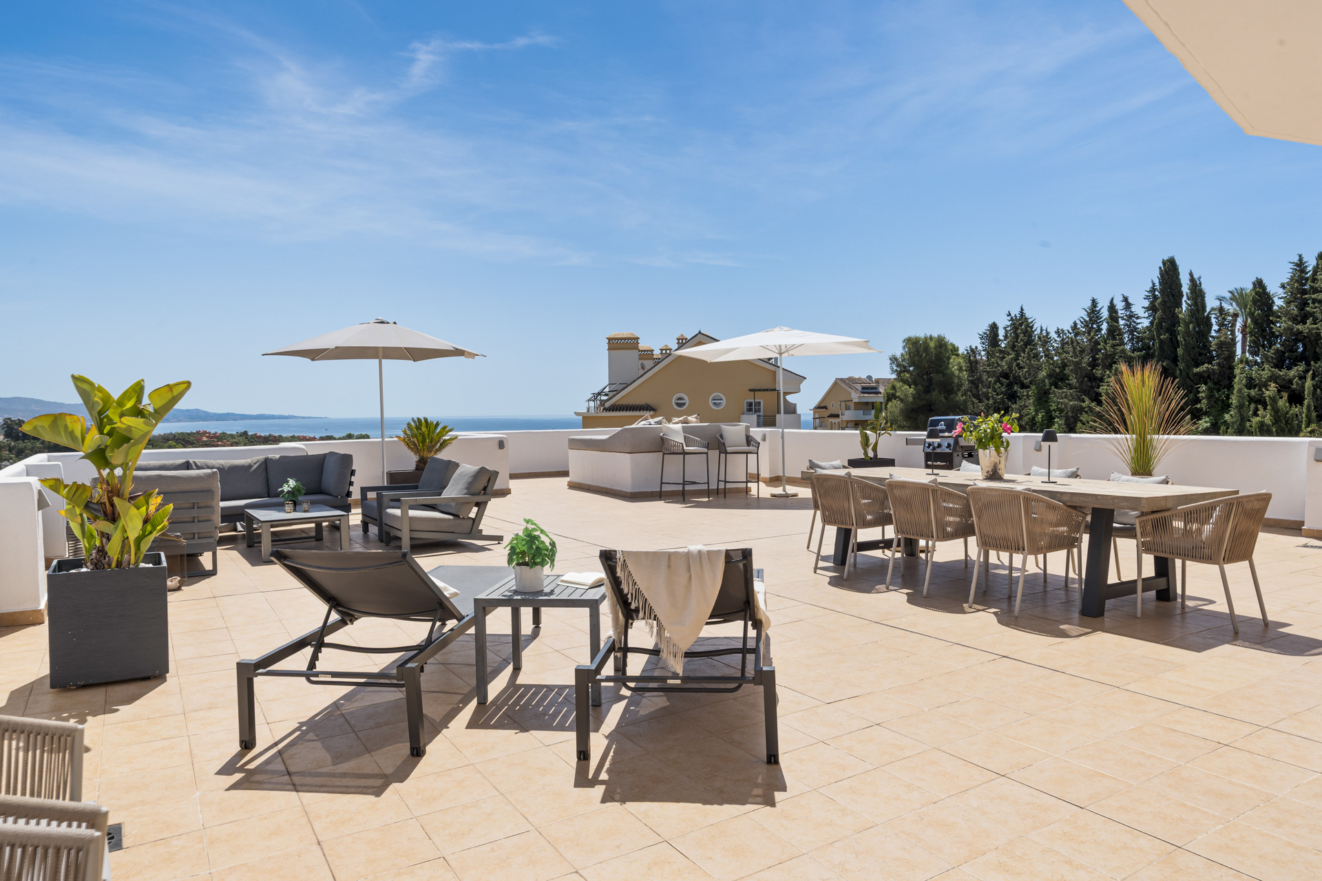 Spacious terrace featuring lounge chairs, dining table, umbrellas, and views of the sea and greenery.