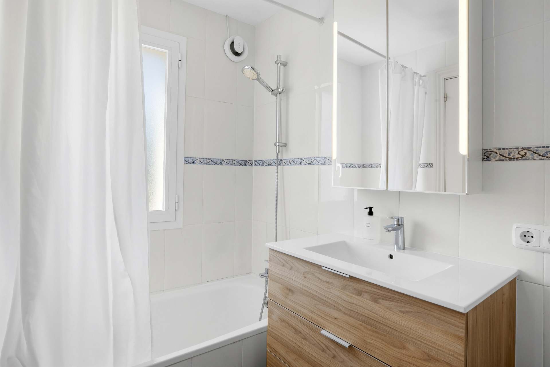 Modern bathroom with a bathtub, shower, and a wooden vanity with a mirror and lighting.