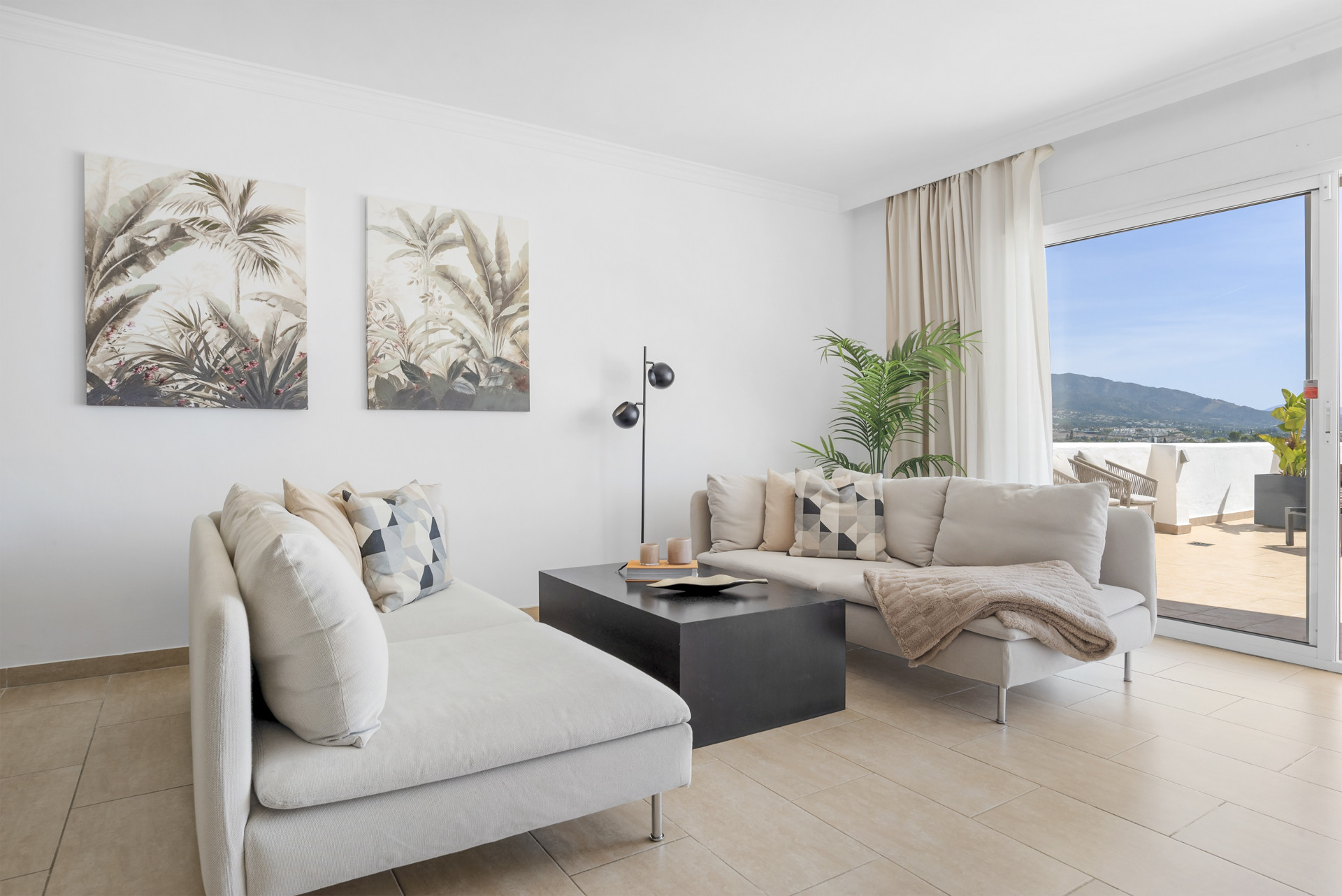 Cozy seating arrangement with two sofas, coffee table, and plants, leading to an outdoor terrace.