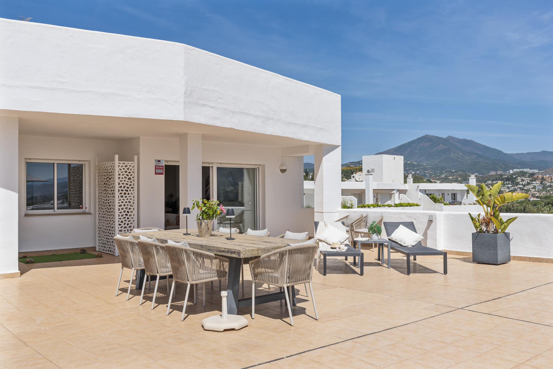 Dining area on the terrace with a large table and additional seating, mountain view in the background.