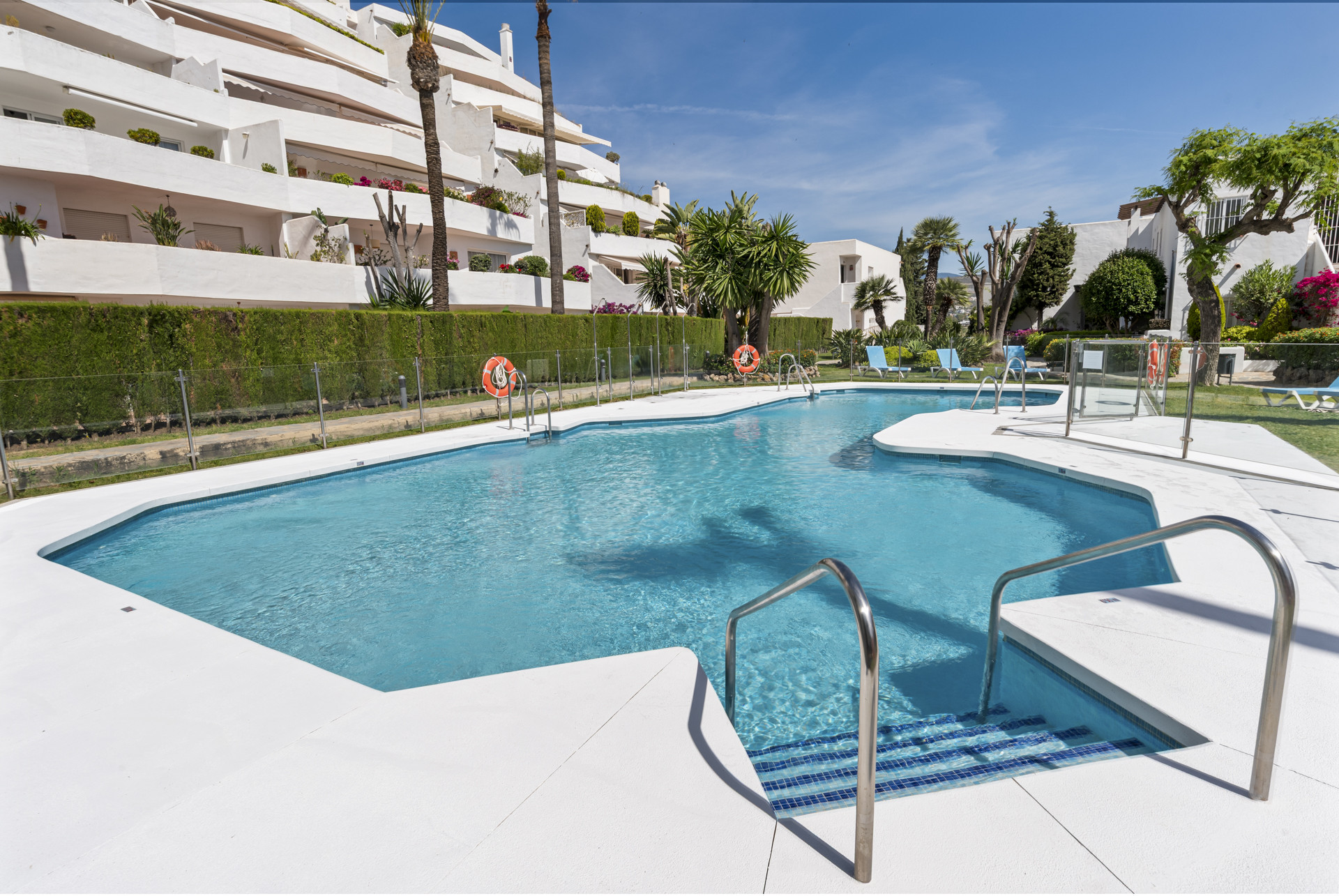 Pool area with steps and lounge chairs surrounded by greenery.