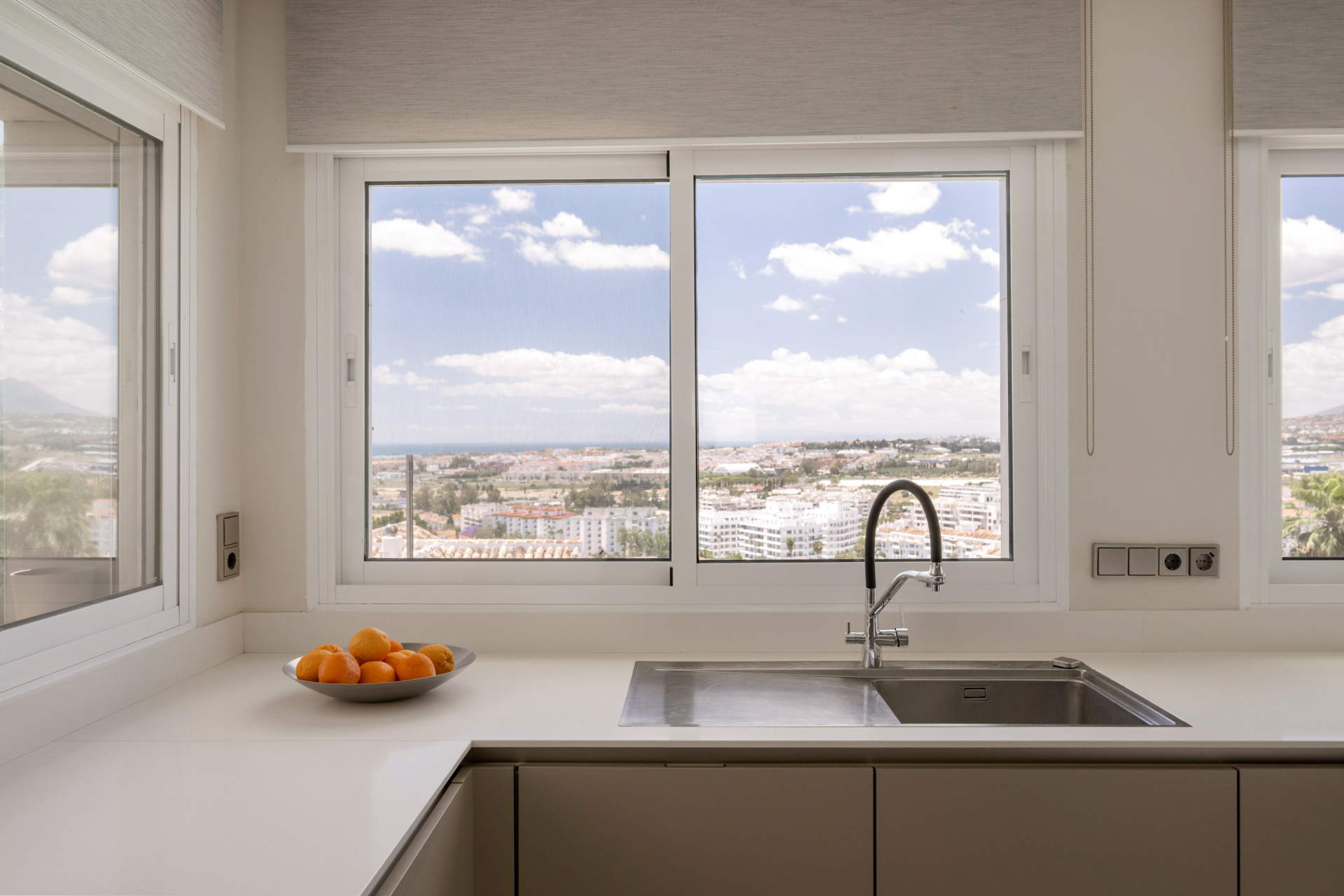 View from kitchen window displaying city and ocean landscapes with fresh fruit on the counter.