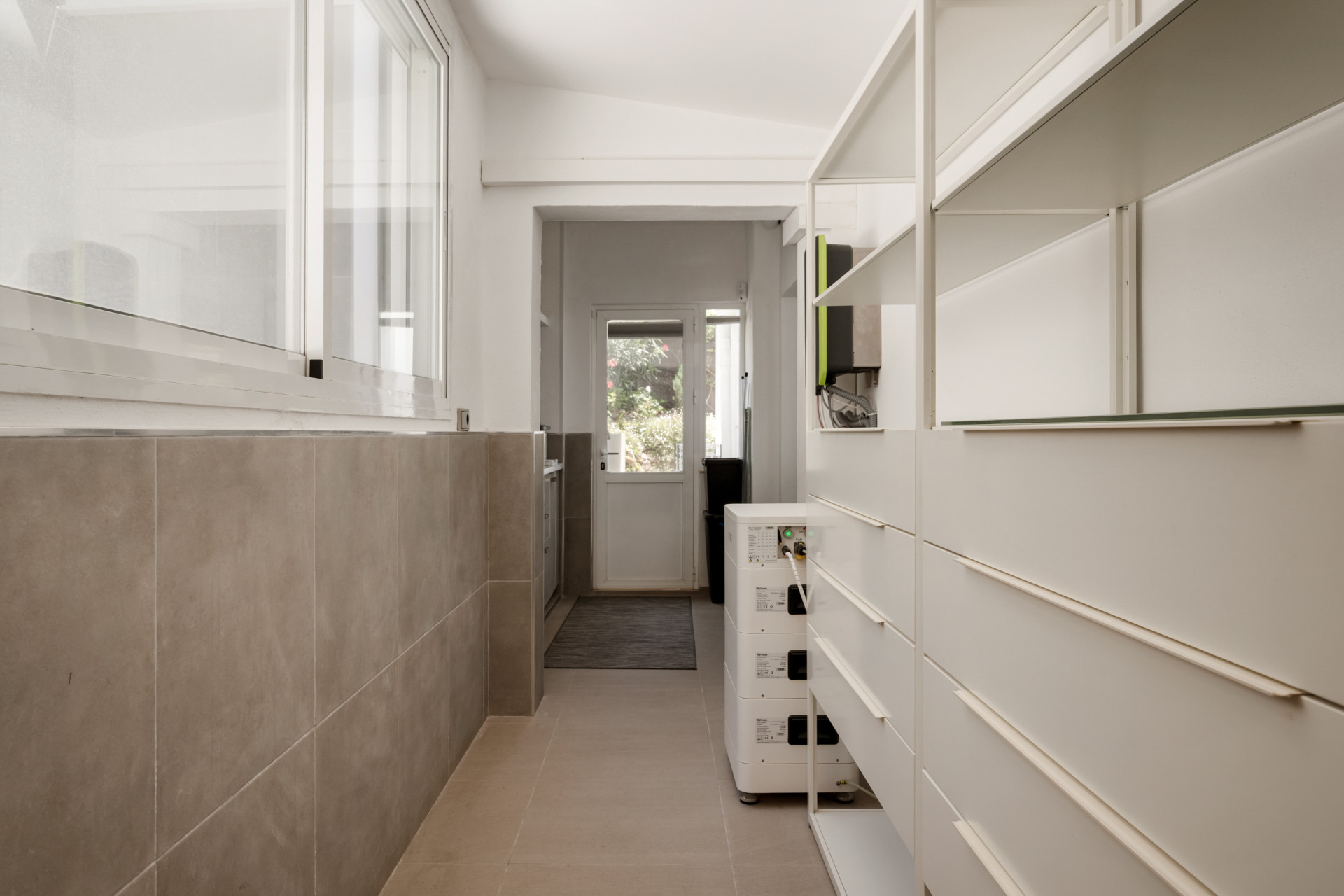 A clean hallway with storage units, light tile flooring, and a door leading outside.