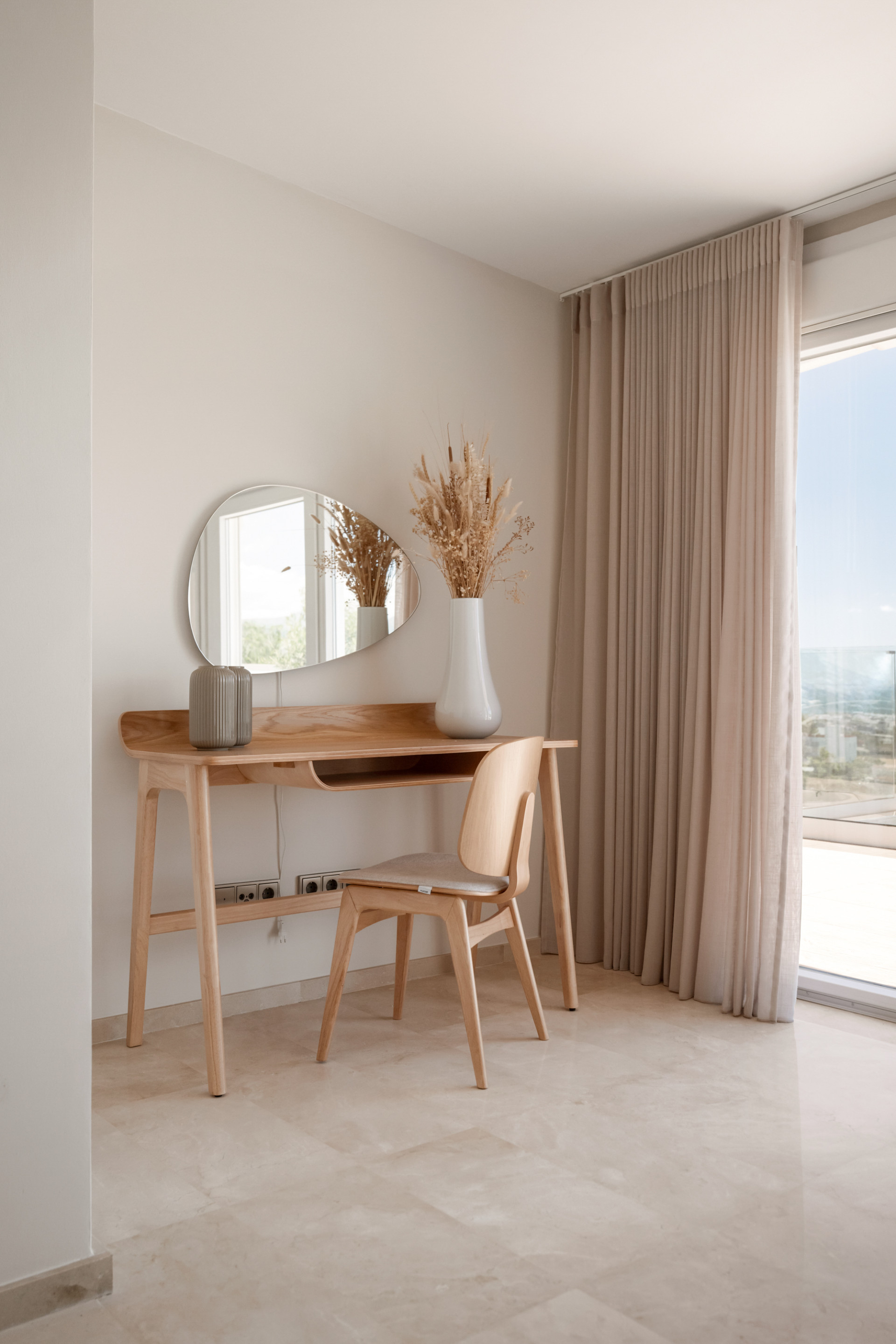 Work desk with a mirror and decorative vase in a well-lit corner by the window.