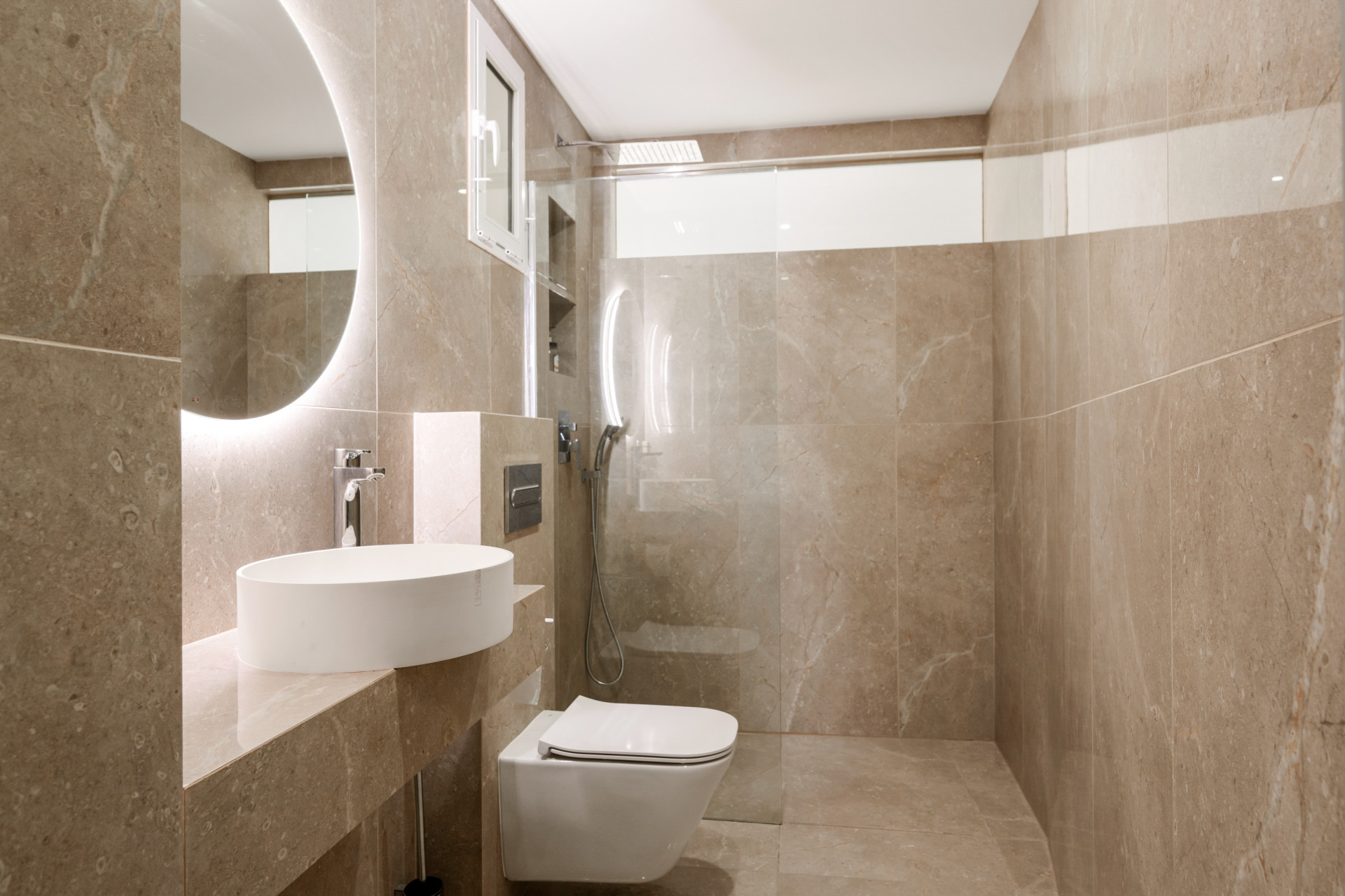Modern bathroom featuring a round sink and marble tile walls.