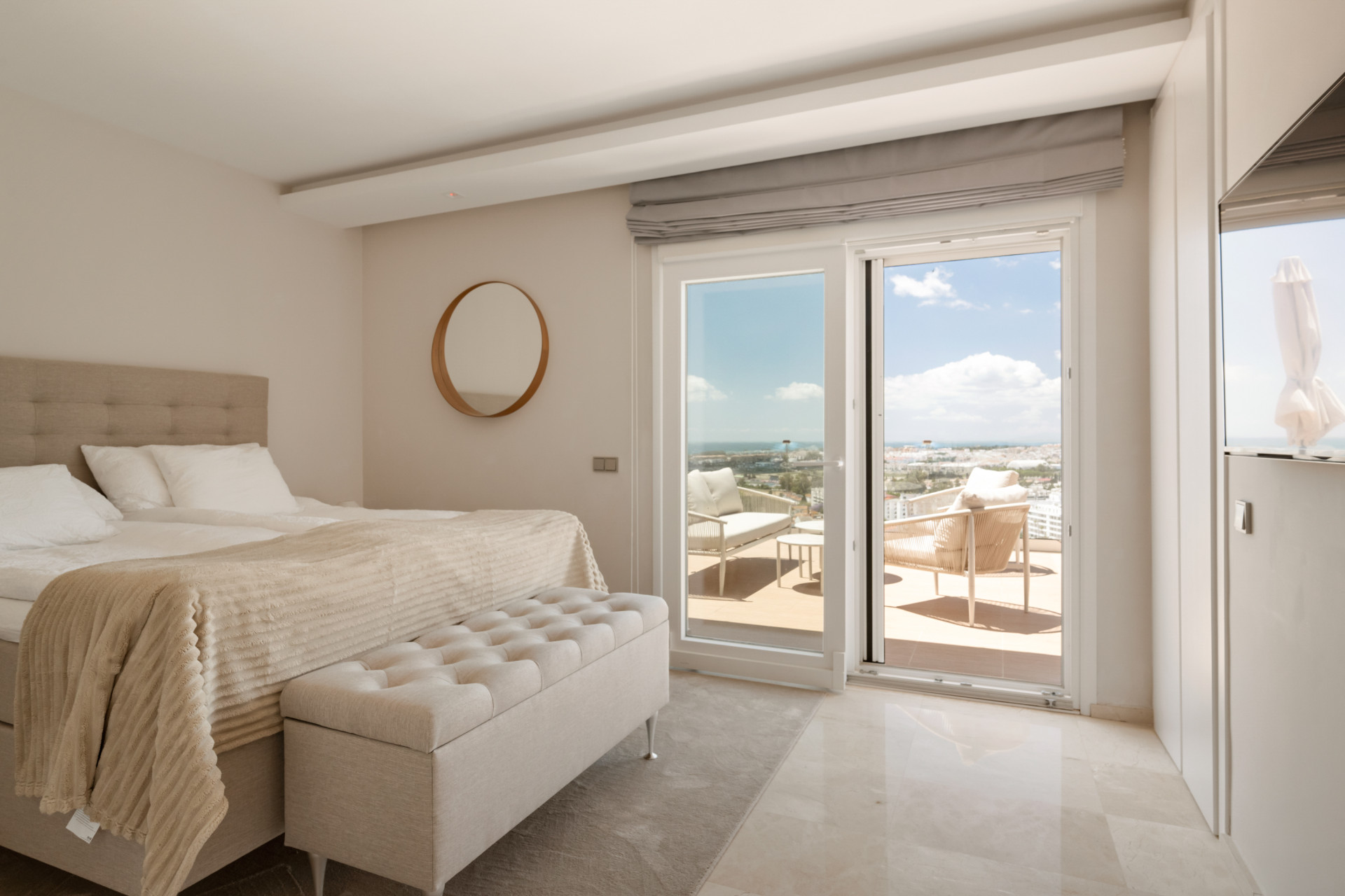 Stylish bedroom with a round mirror, bed, and views through sliding doors.