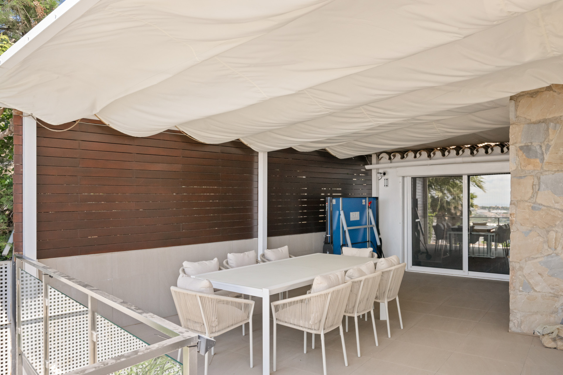 Outdoor dining area with a large table and stone wall accents under a canopy.