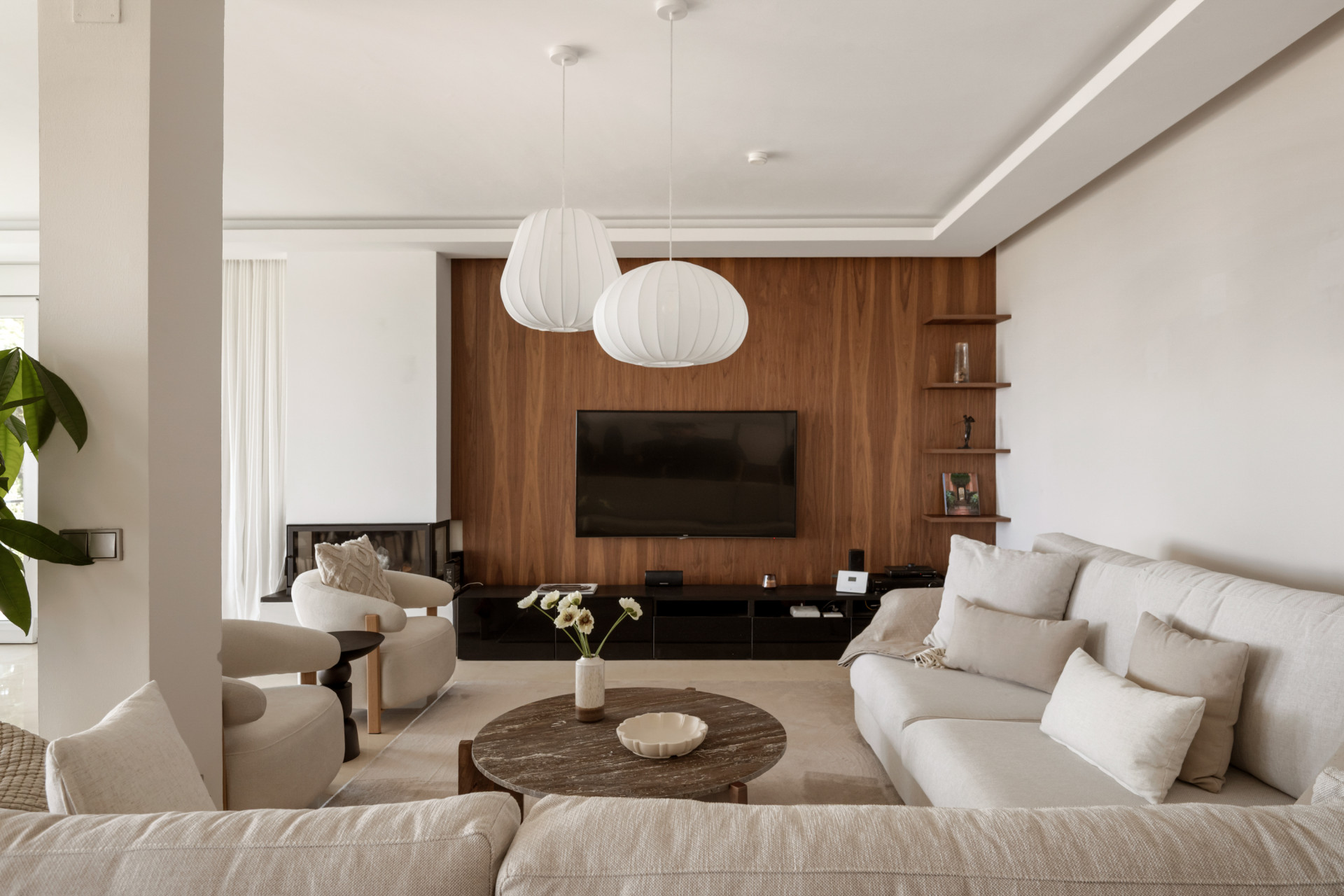 Modern living room with a wooden accent wall, TV, and two hanging light fixtures.