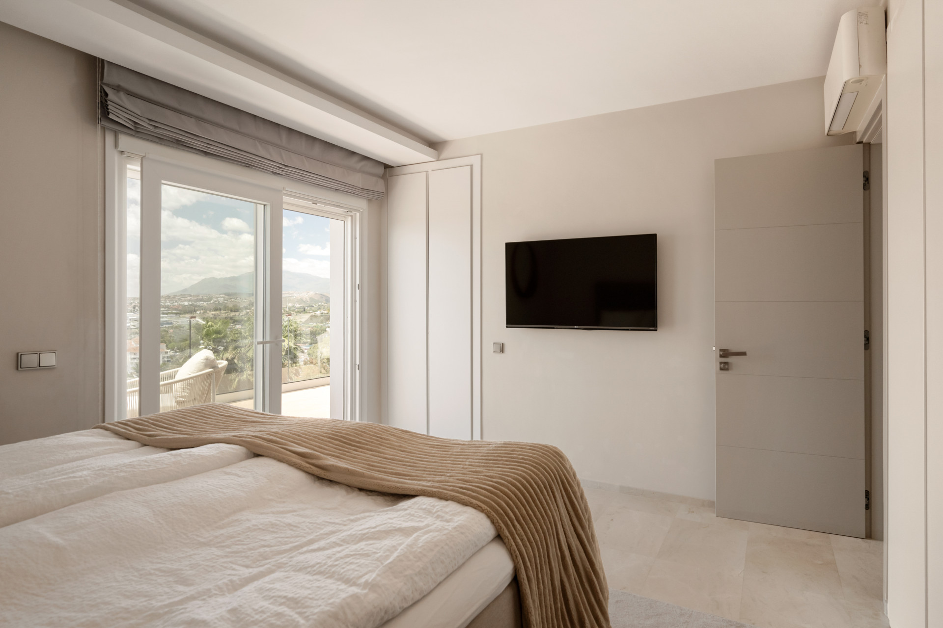 Bright bedroom with a view, featuring a bed, TV, and sliding doors to a terrace.