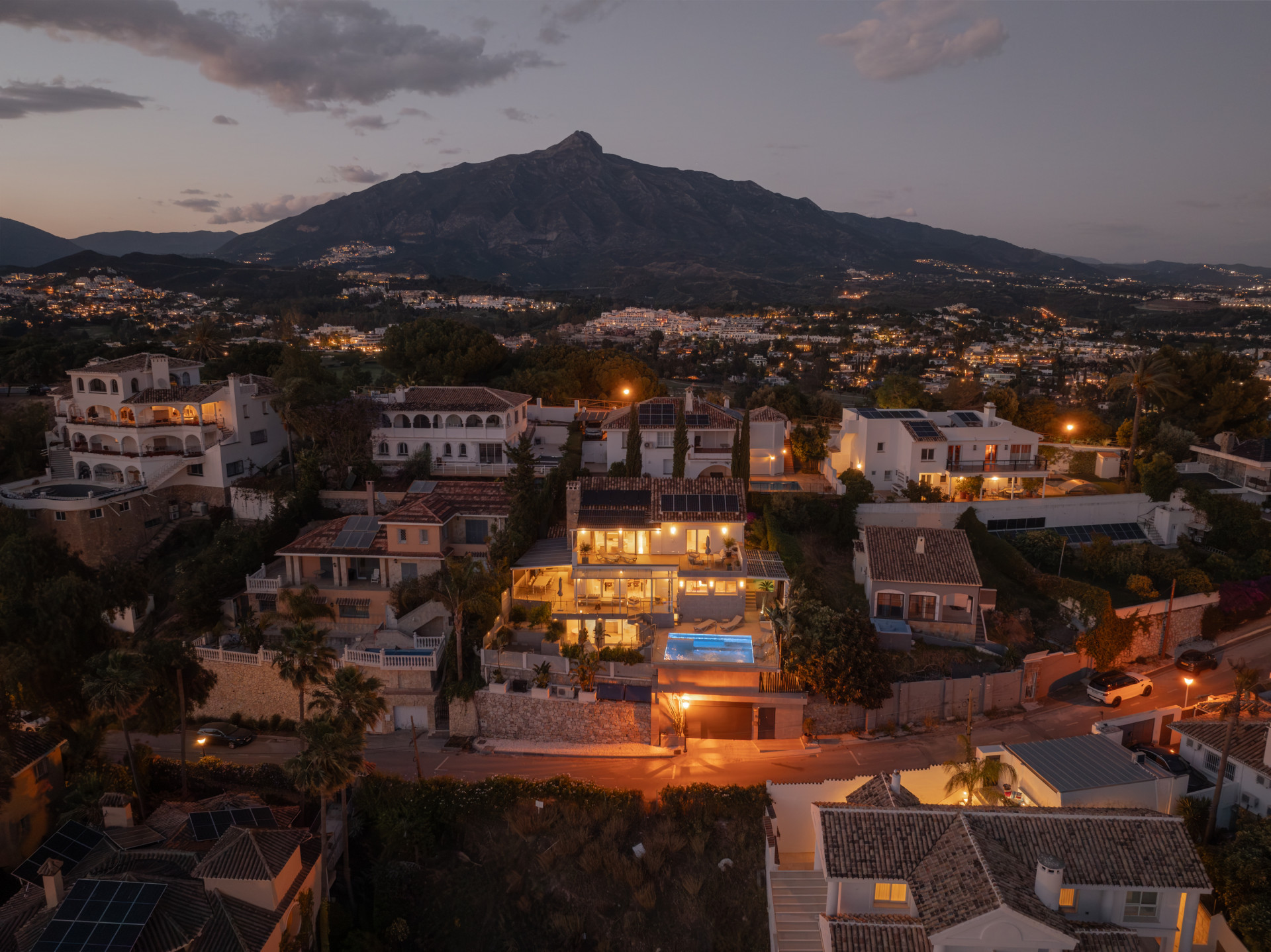 Aerial view of the villa at night, highlighting the pool and surrounding mountain landscape.