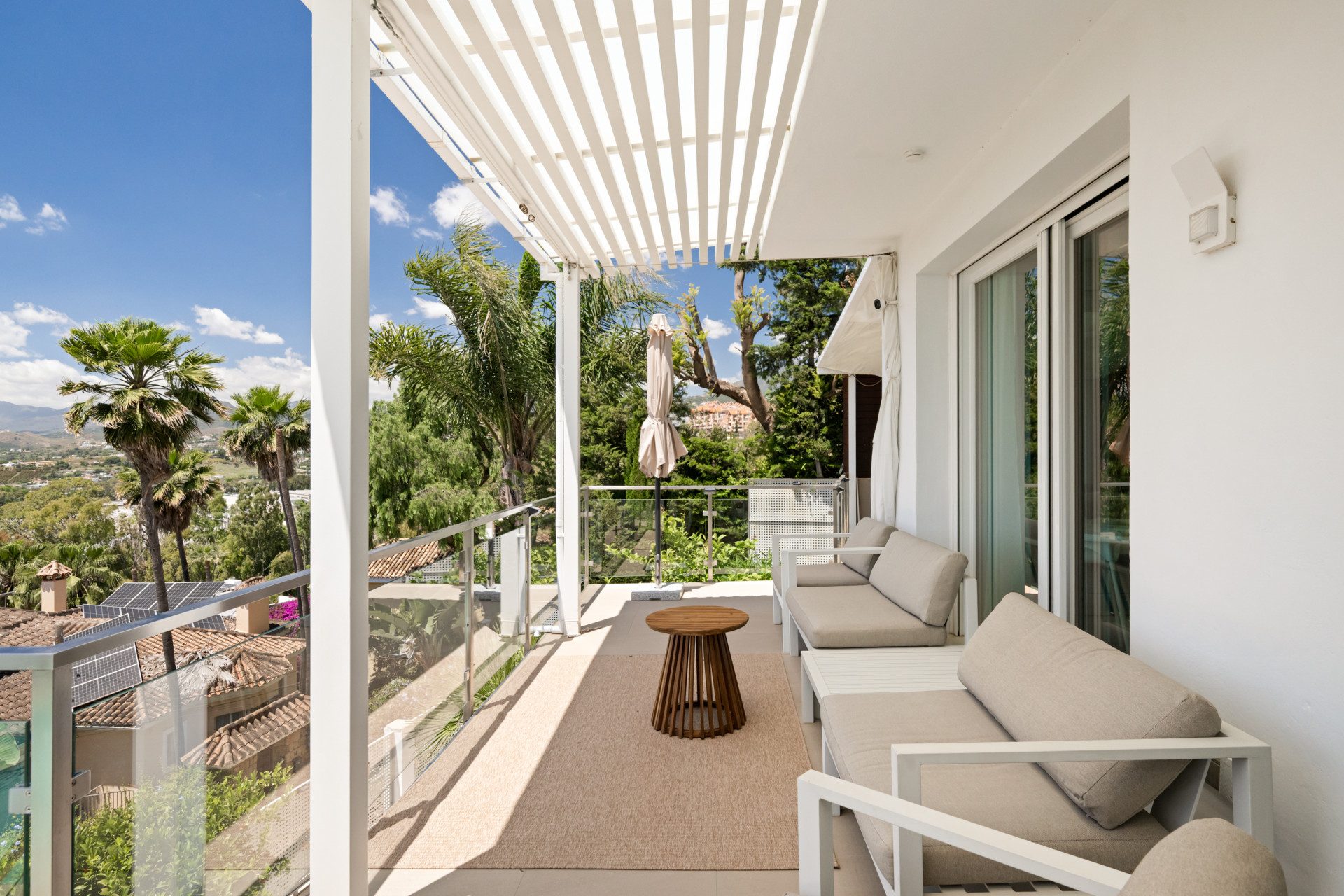 Covered terrace with seating and a coffee table overlooking palm trees and mountains.