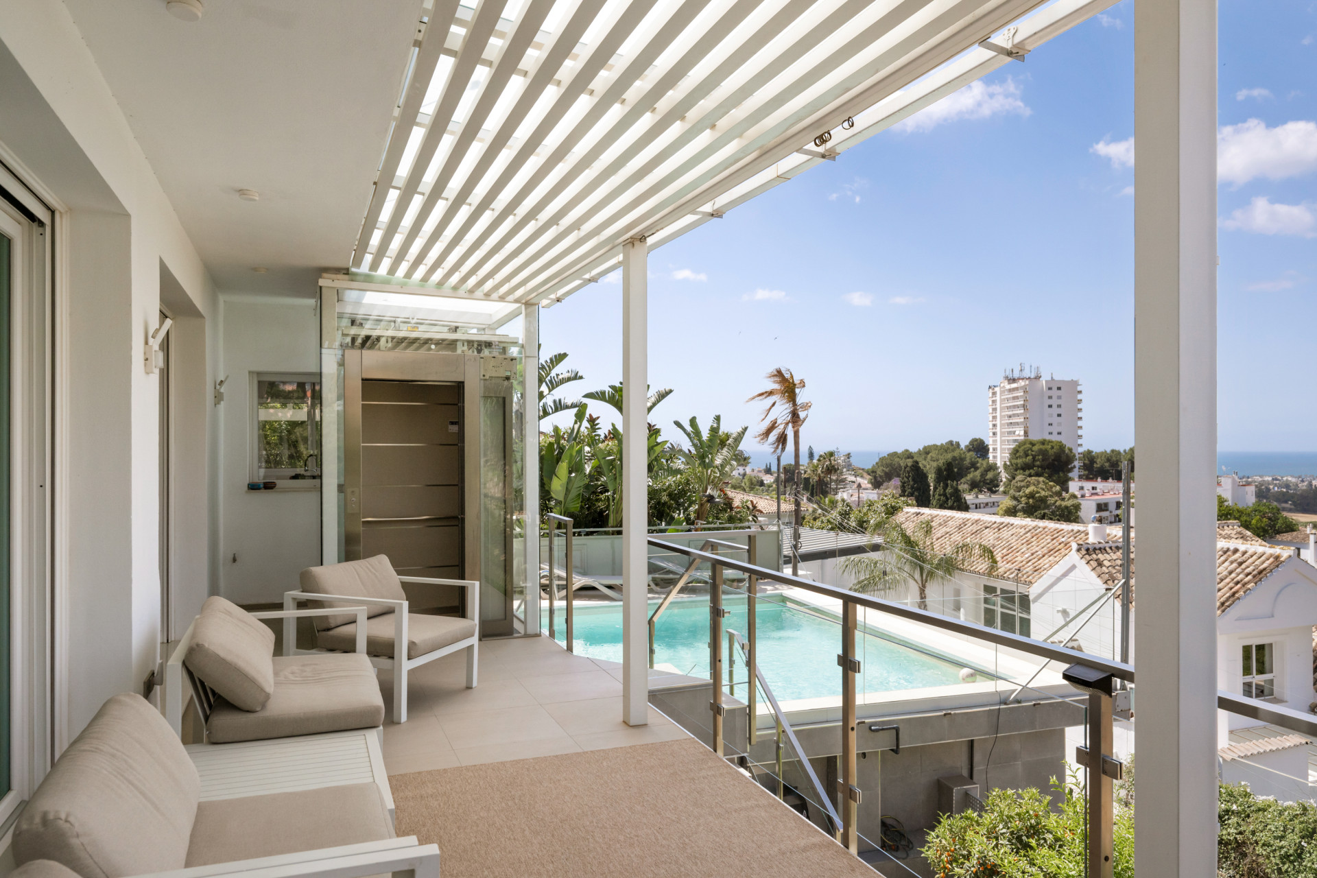 Covered terrace with seating area overlooking a pool and greenery.