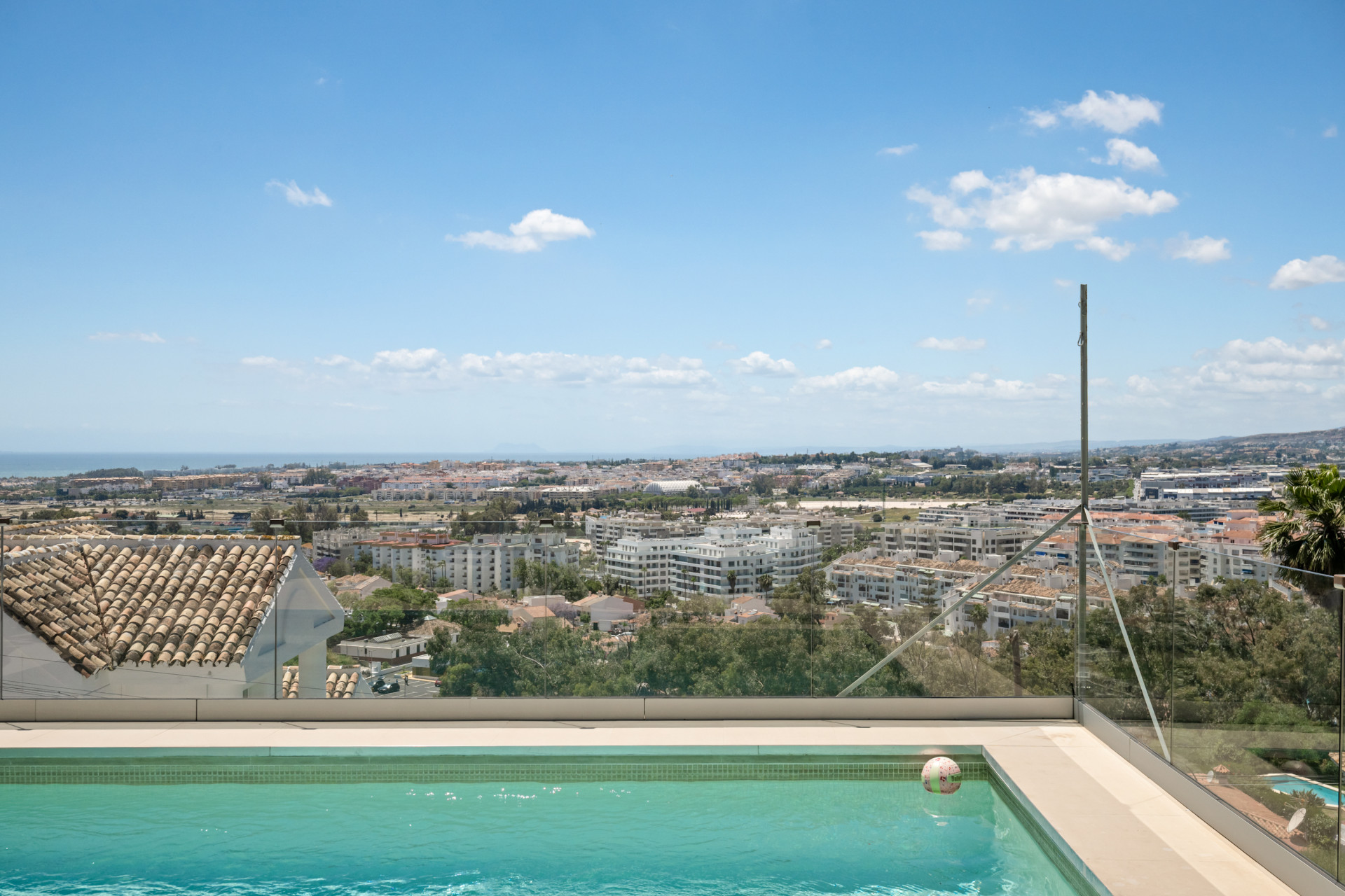 A panoramic view from a poolside overlooking the city and coastline under a clear blue sky.