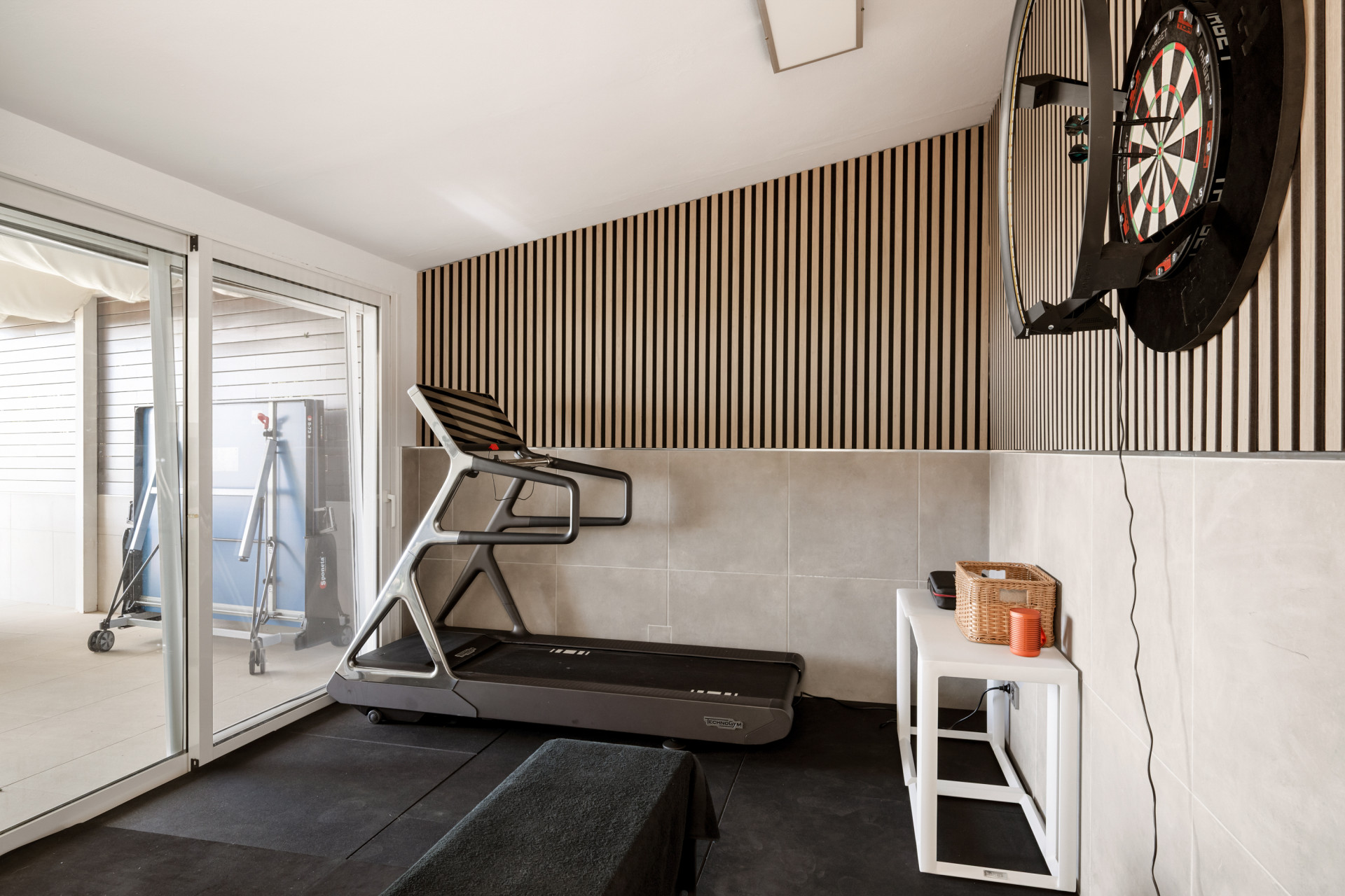 A fitness room featuring a treadmill, dartboard, and striped wall details.