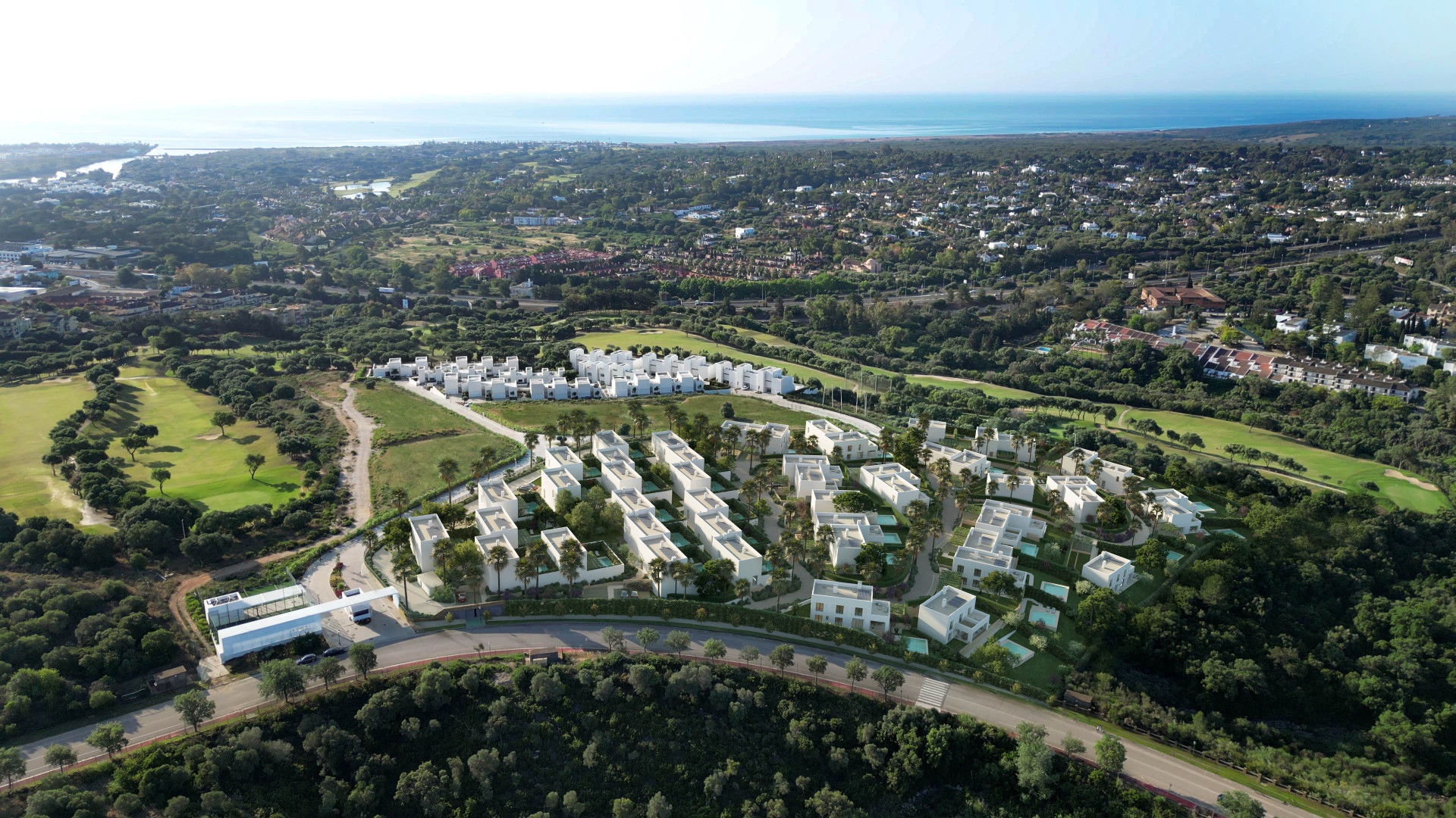 Aerial view of a community of white modern villas with pools, surrounded by green golf courses and ocean.