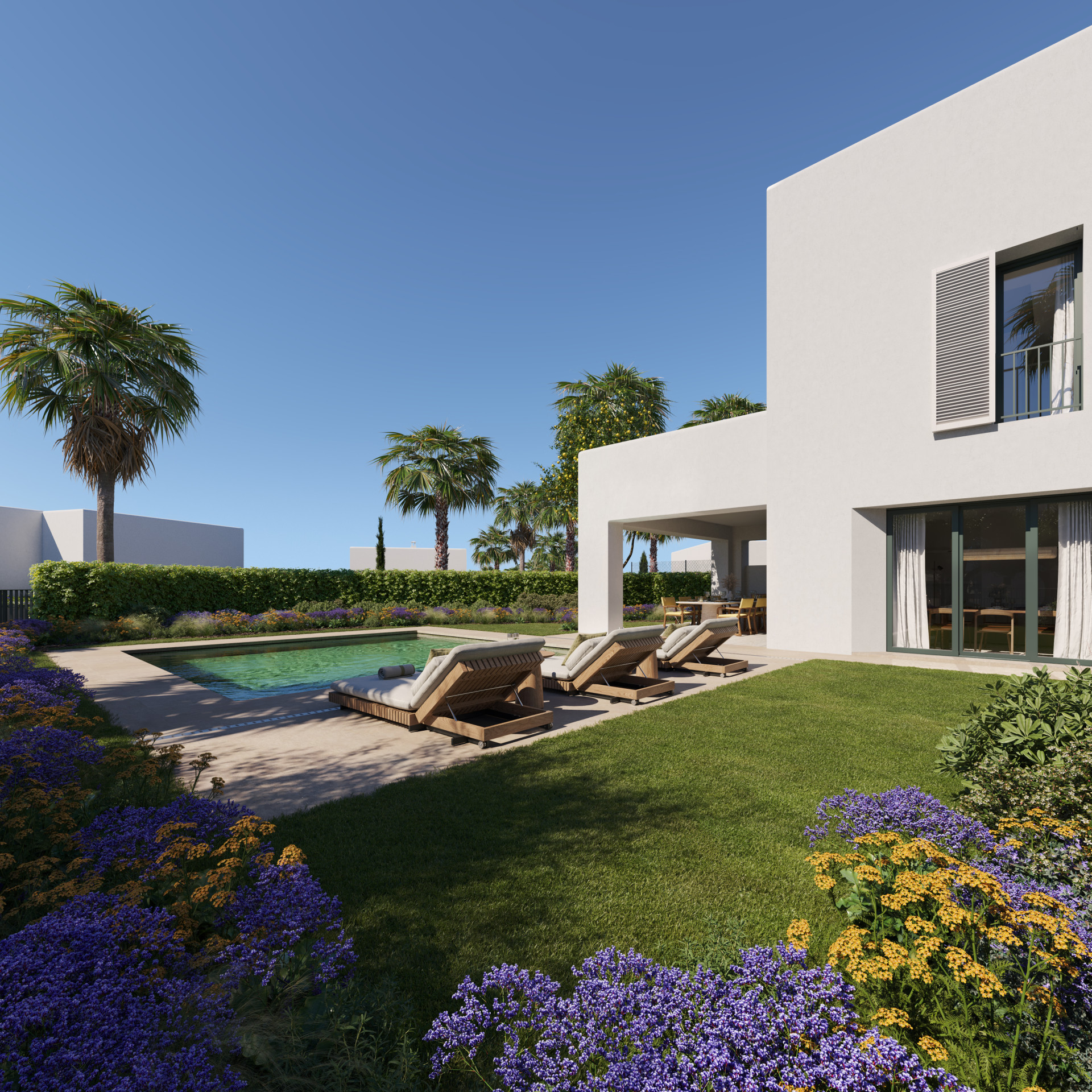 Villa backyard with a rectangular pool, wooden lounge chairs, green lawn, colorful flower beds, and palm trees.