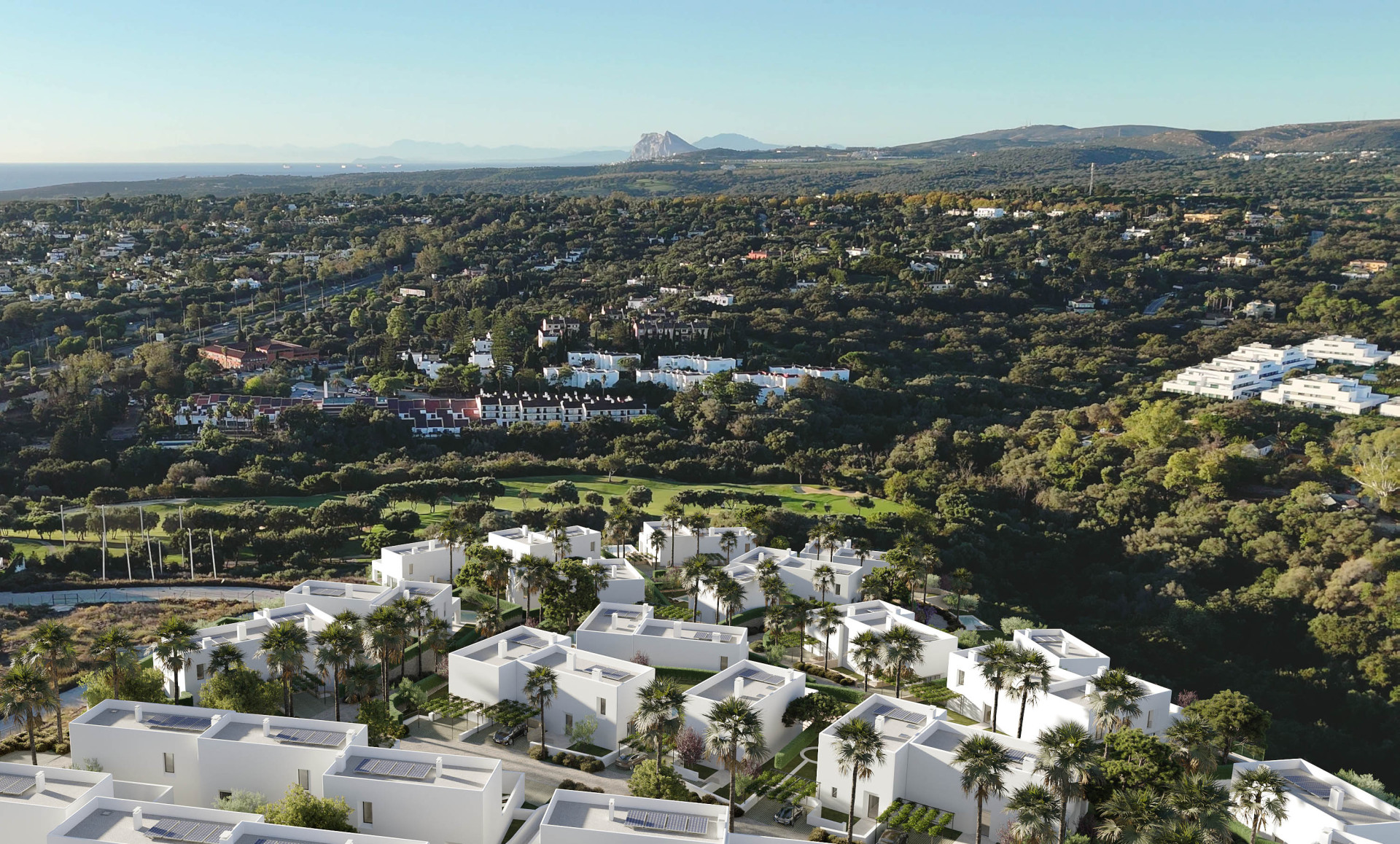 Drone view of a white villa community with palm trees, green hills, and the Rock of Gibraltar in the distance.