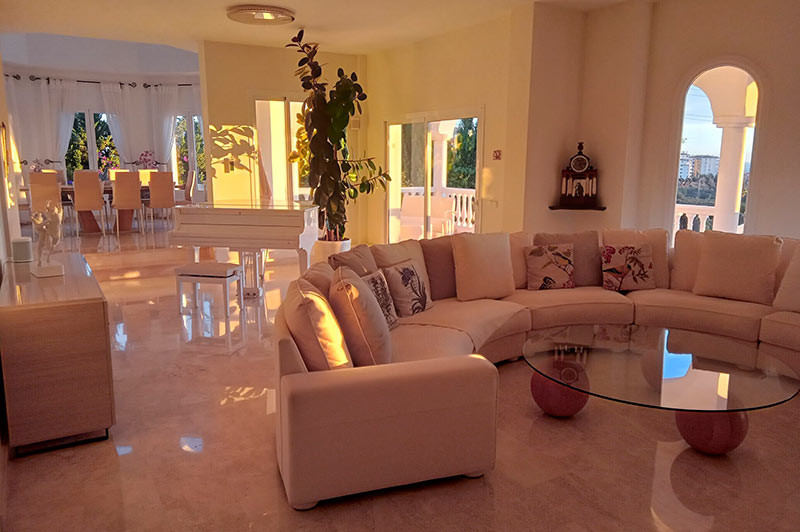 Spacious living area with a cream curved sofa, glass coffee table, and sunset light streaming in.