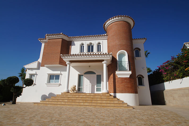 Exterior of a large house with white walls, red brick accents, a tower, and a grand entrance staircase.