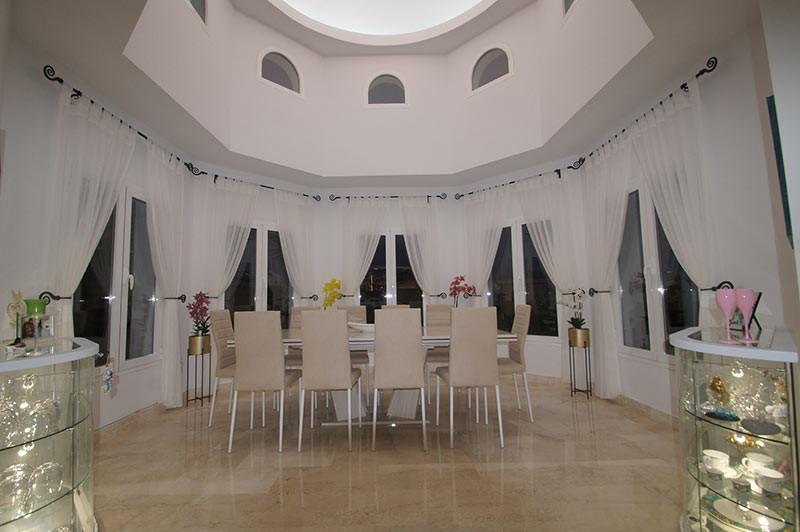 Formal dining room with a long table, ten chairs, large arched windows, and a high domed ceiling.