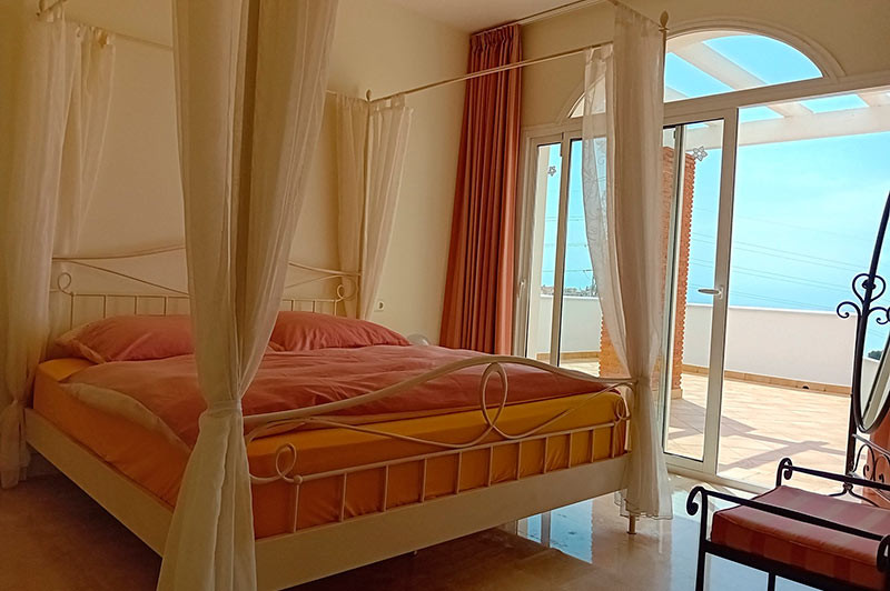 Bedroom with a white canopy bed, red bedding, and a glass door opening to a terrace with a view.