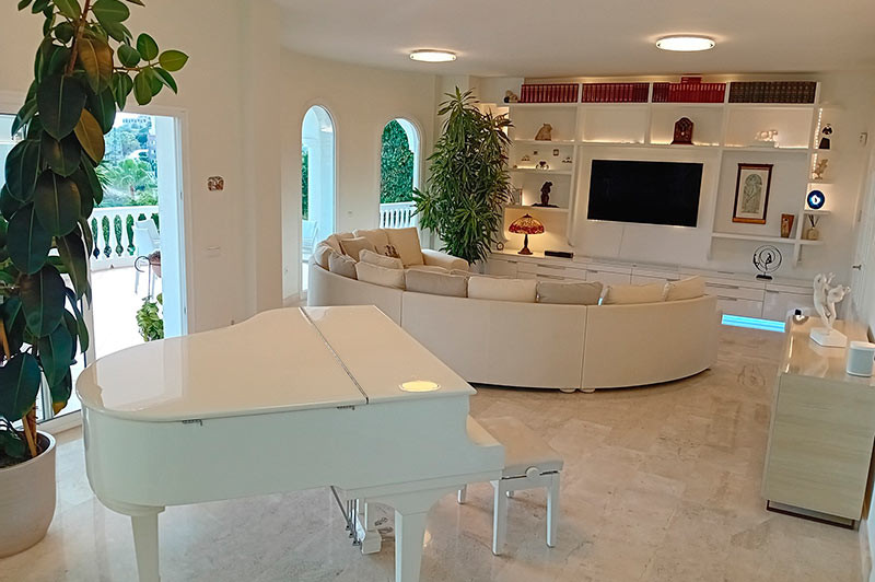 Living room with a white grand piano, curved sofa, built-in entertainment unit, and large plant.
