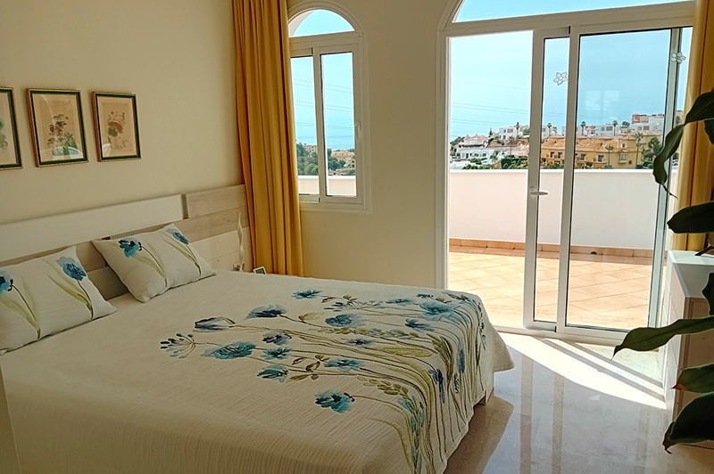 Bedroom with a bed, yellow curtains, and an open glass door leading to a tiled terrace.