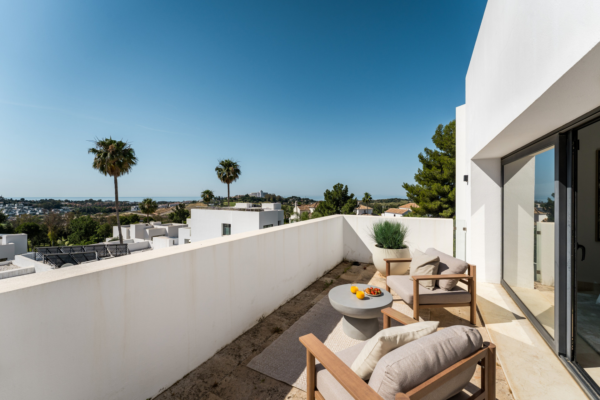 Outdoor terrace featuring seating and a view of palm trees and the coast.