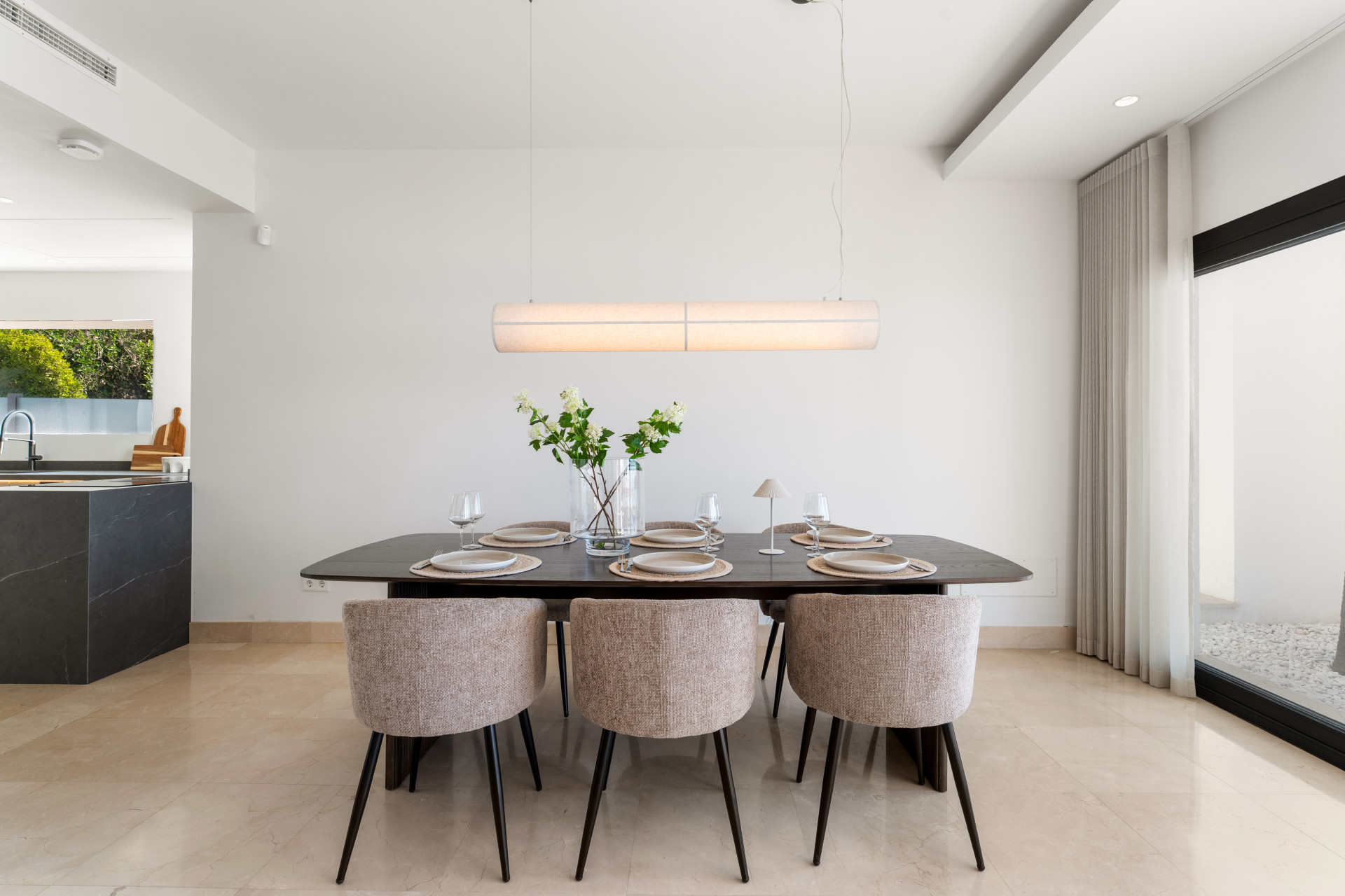Dining area with a large table, beige chairs, and a hanging light fixture.