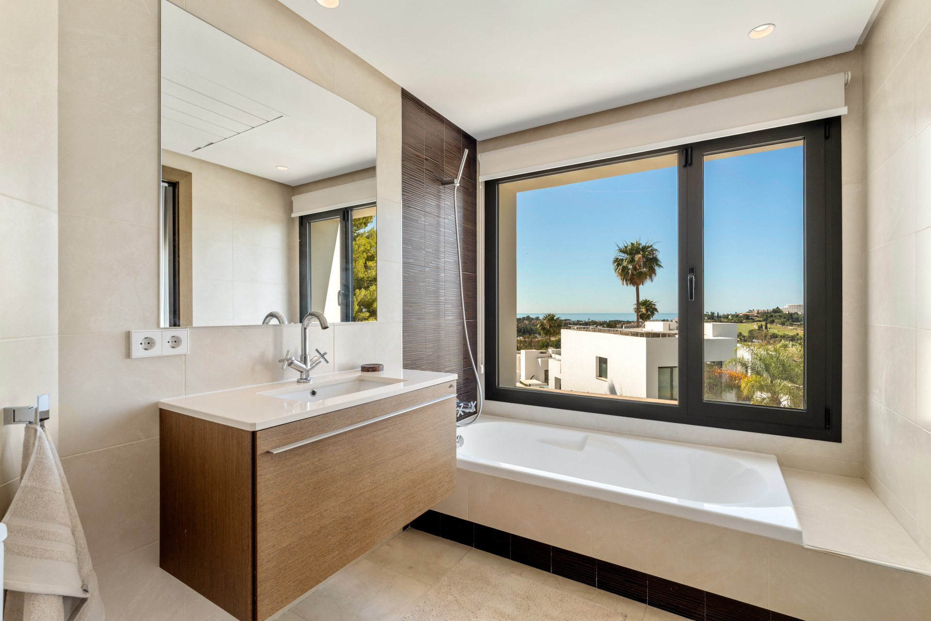 Modern bathroom with bathtub, shower, and large window featuring palm tree views.