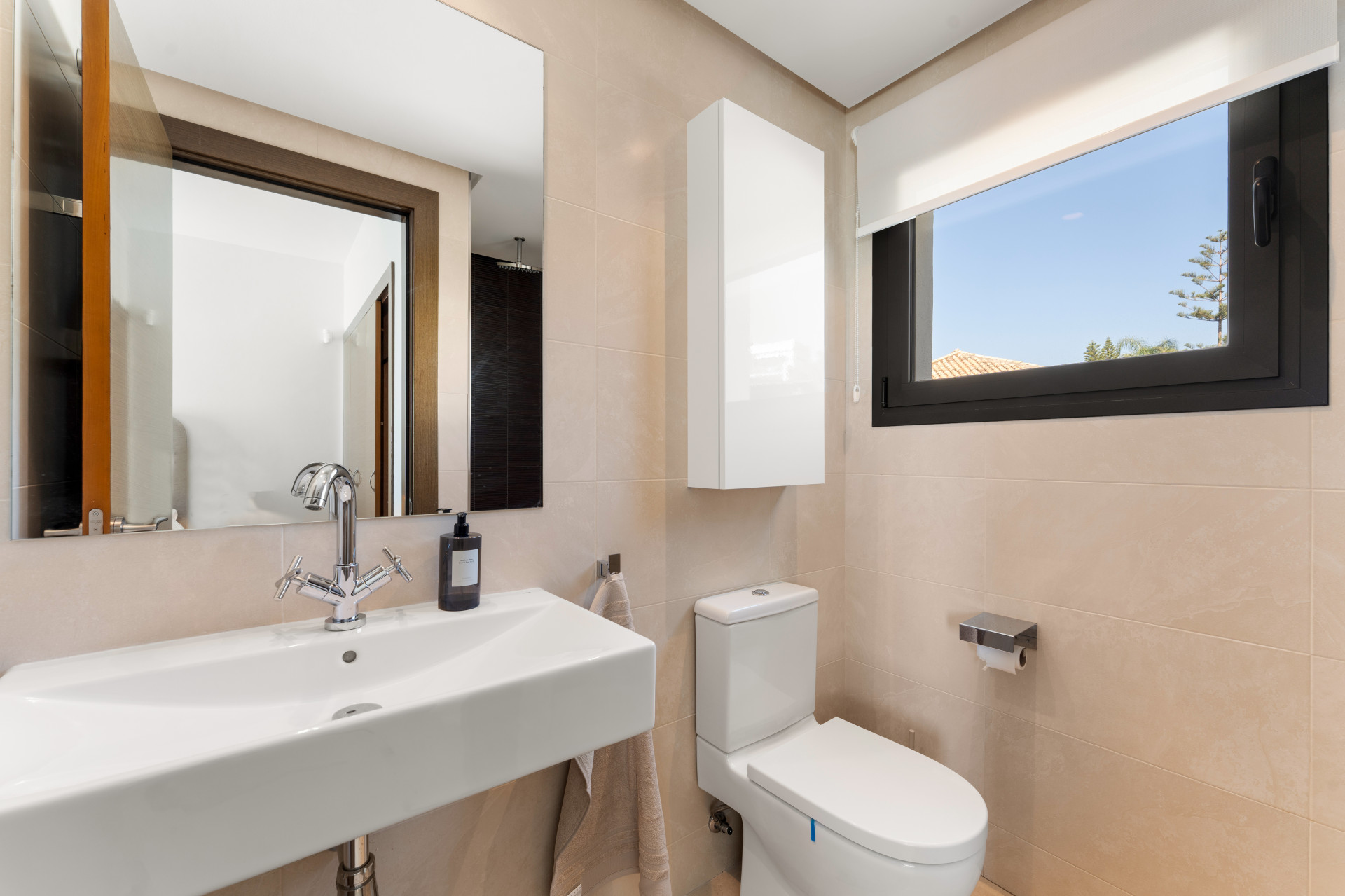 Compact bathroom with a sink, toilet, and window overlooking greenery.